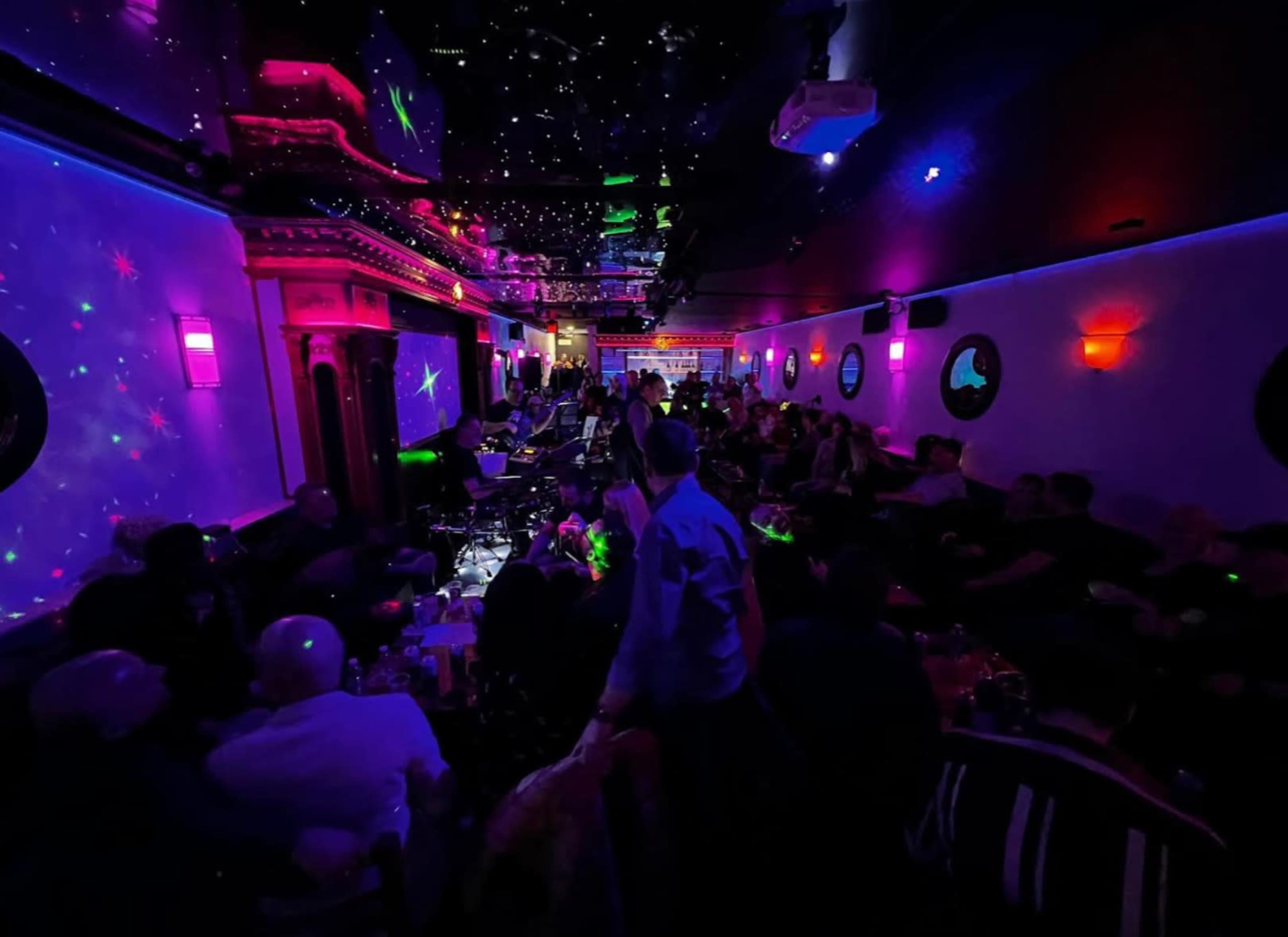 A crowded nightclub features colorful lighting and a live band performing on stage.