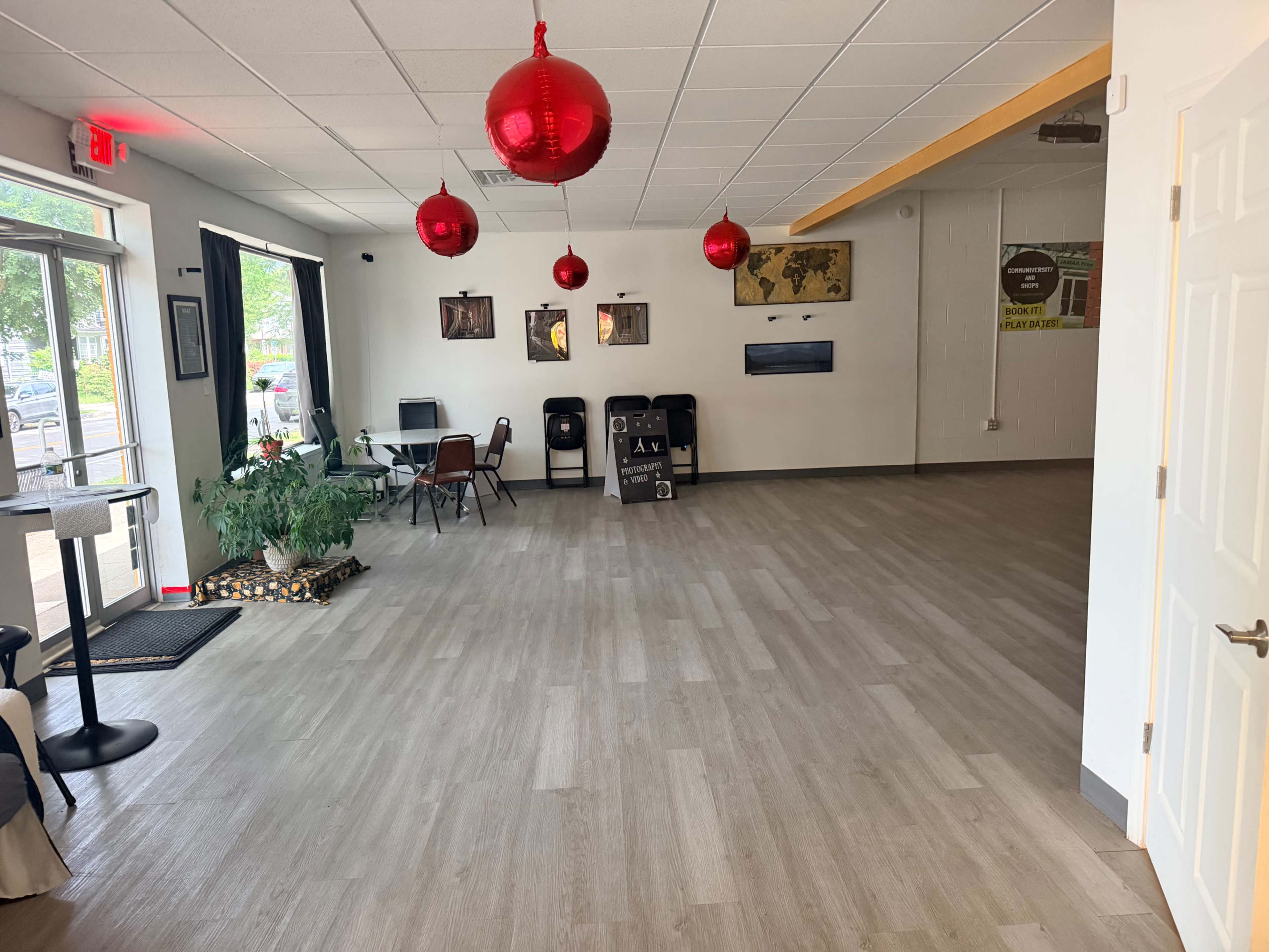 The image shows an empty indoor space with wooden flooring, a few chairs and tables, and red lanterns hanging from the ceiling.