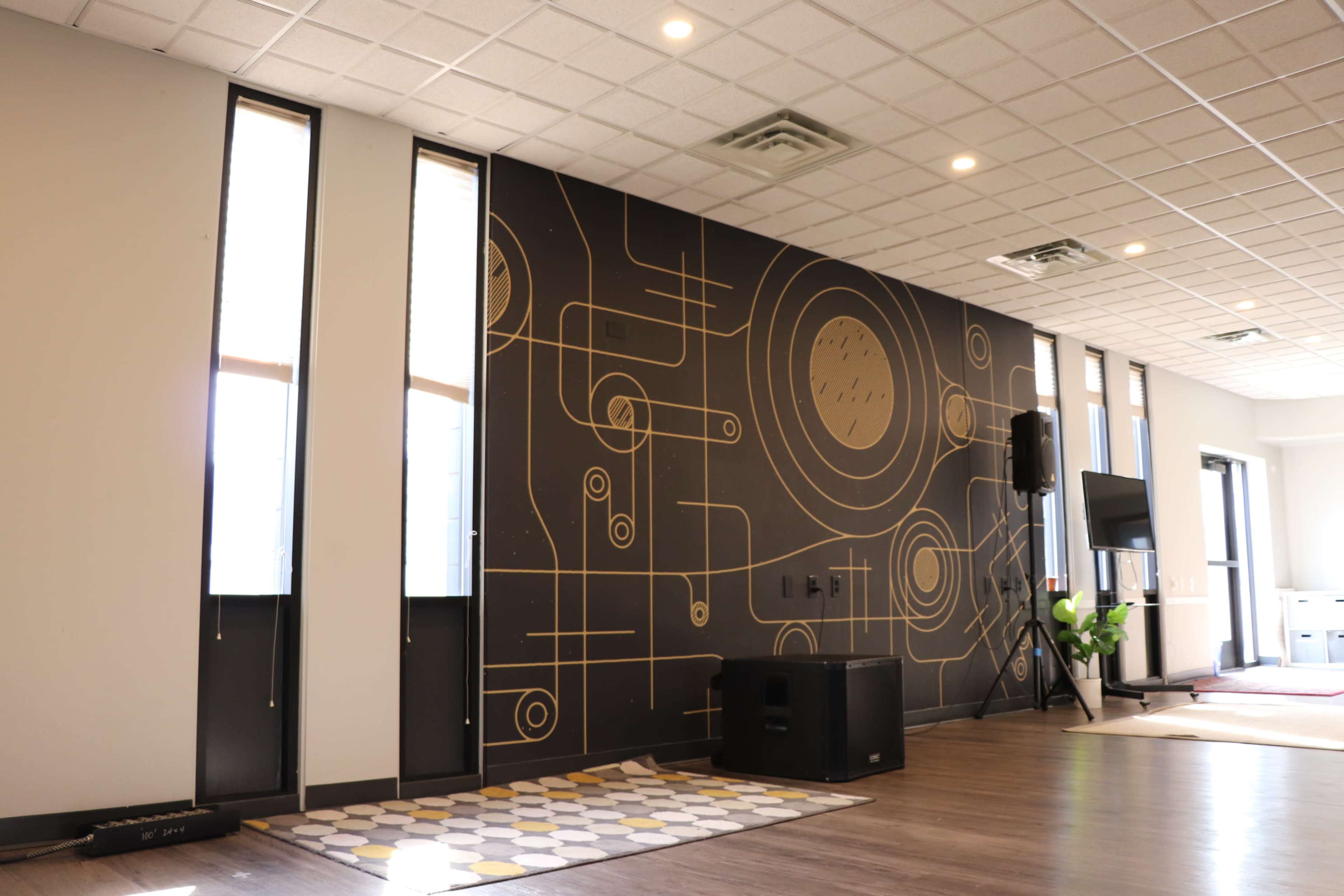 The image shows a modern interior space featuring a geometric patterned wall mural, large windows, and a sound system in the corner.