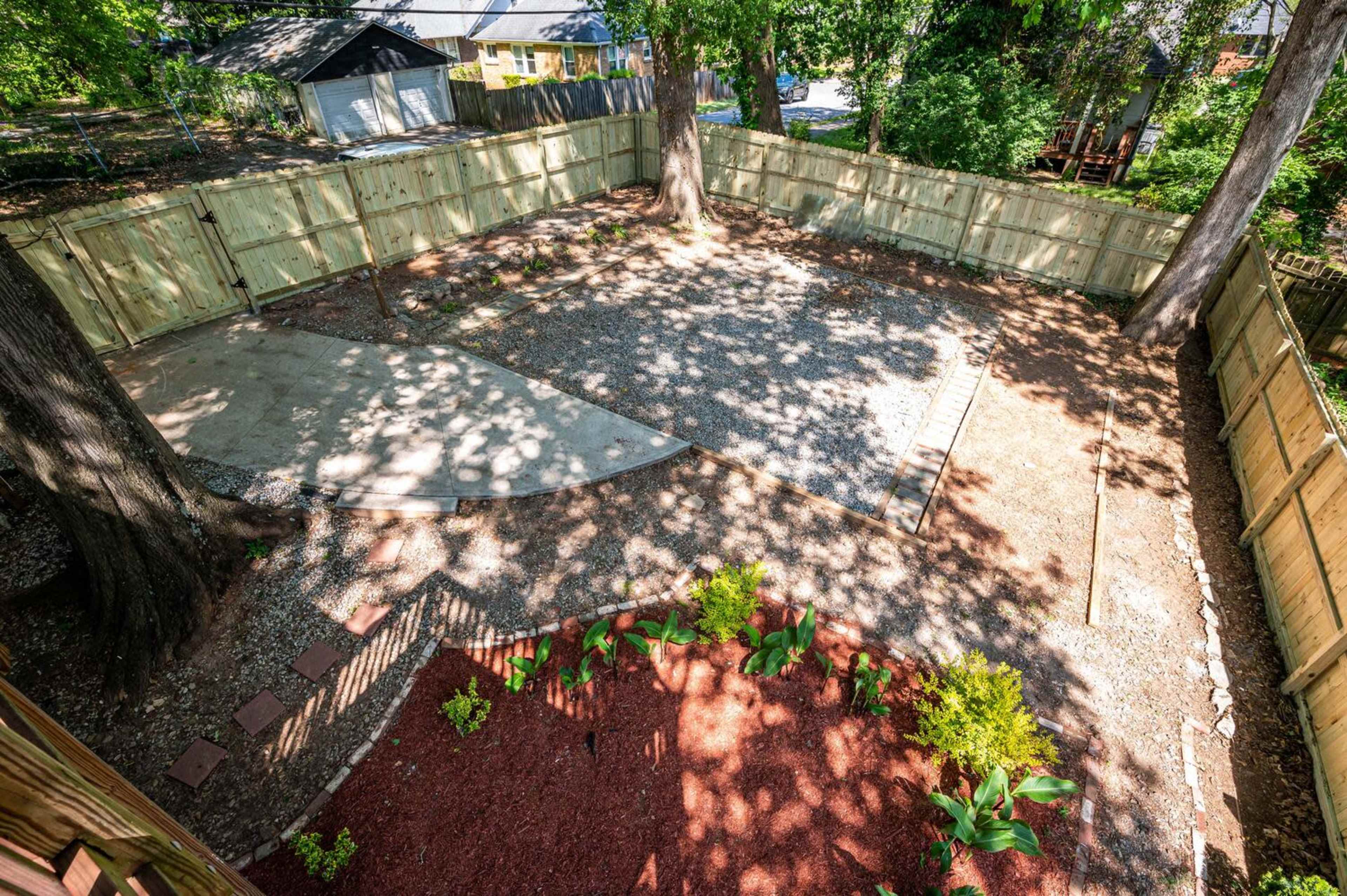 A fenced backyard with gravel areas, a small concrete slab, and garden beds with plants.