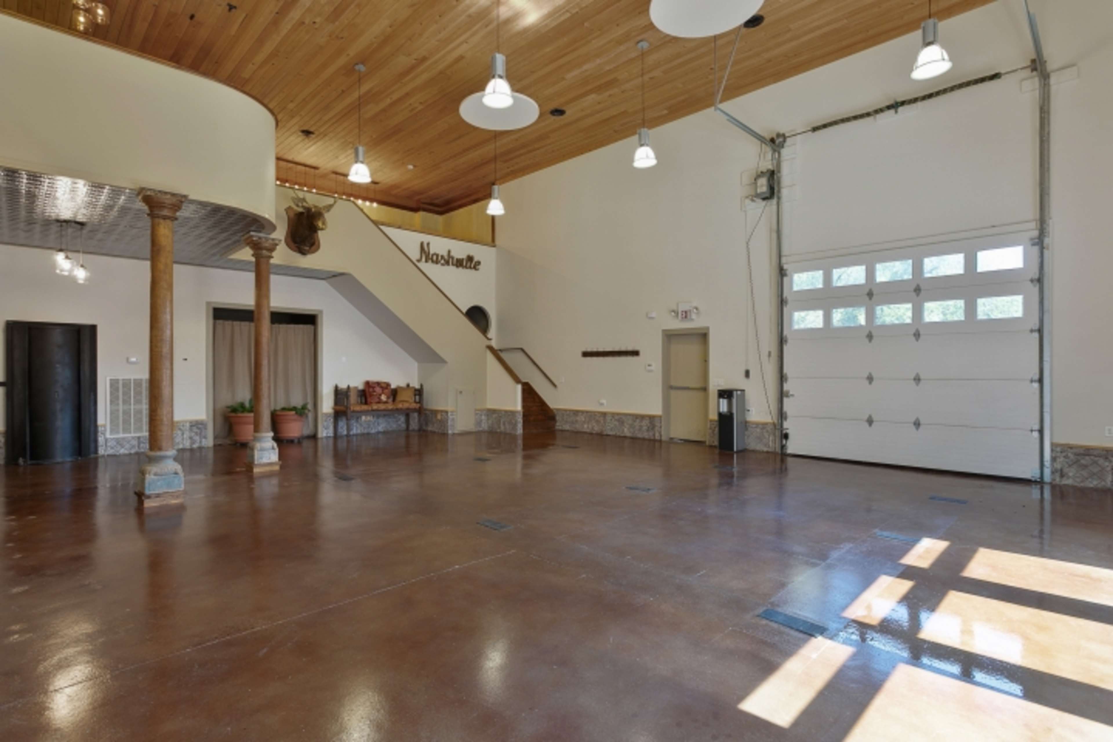 The image shows an open interior space featuring a polished concrete floor, wooden ceiling, and a large garage door.