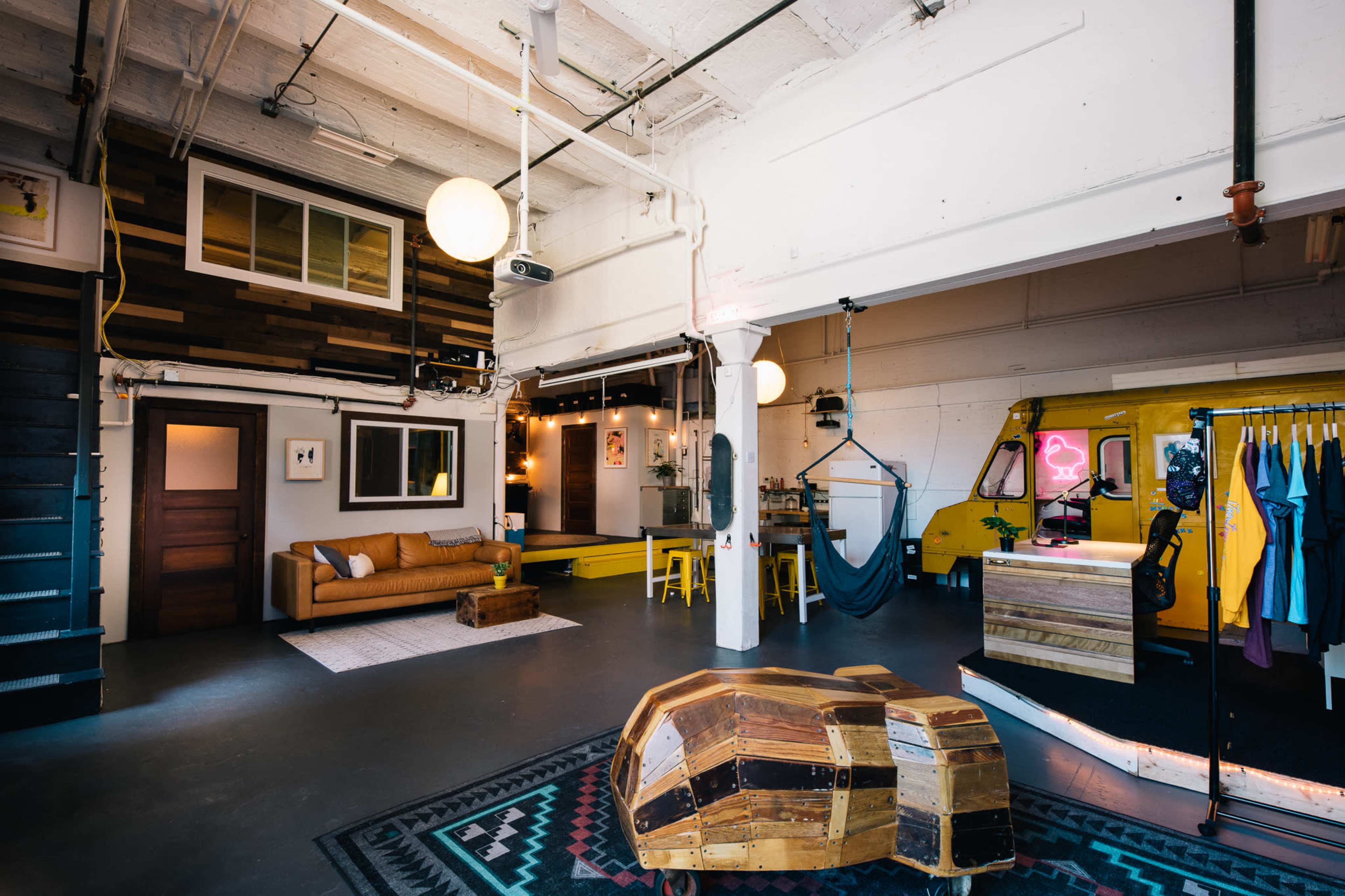 An open-plan workspace featuring a cozy sitting area with a couch, a small reception area with a vintage vehicle, and a clothing display rack.