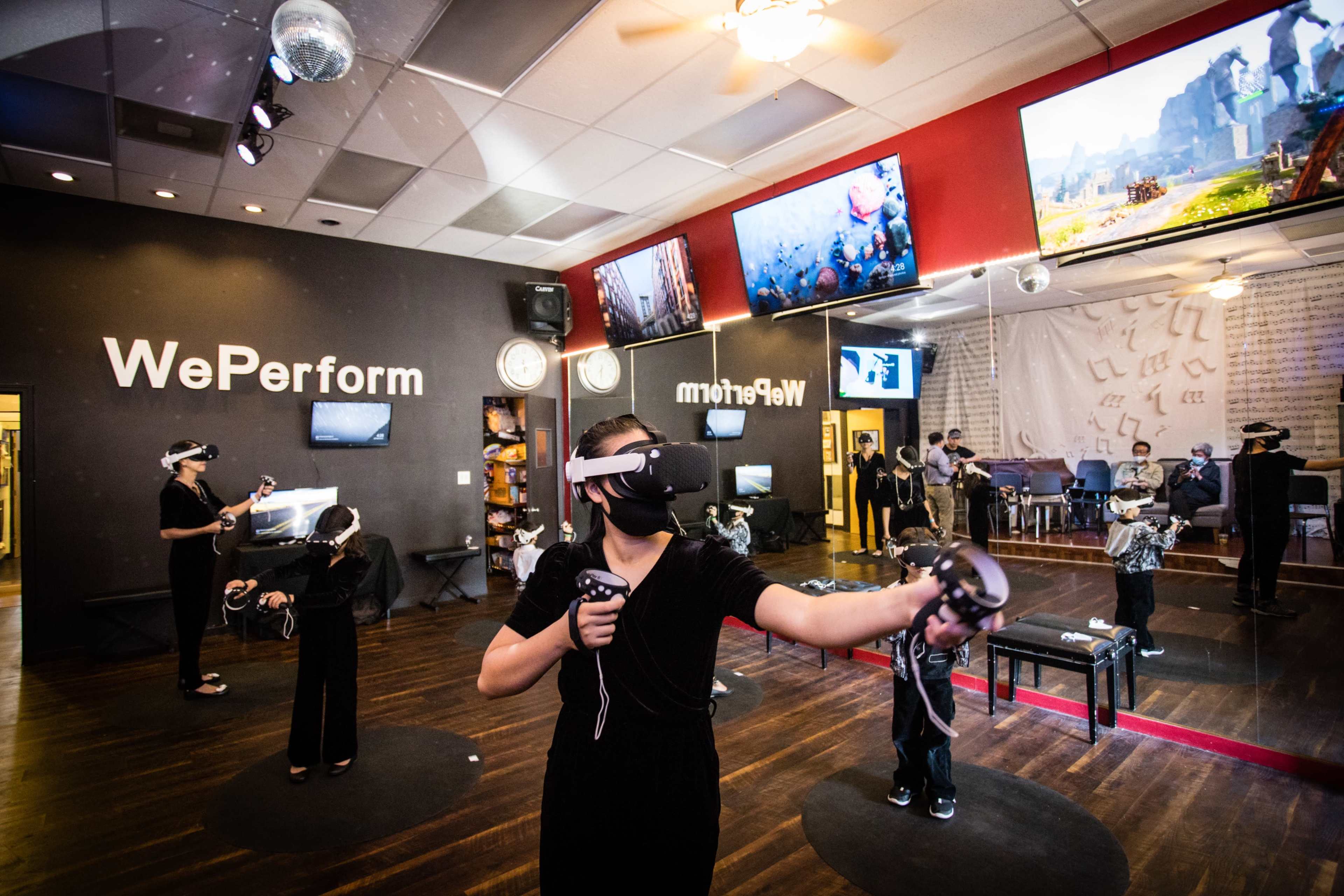 A group of people wearing virtual reality headsets engage in immersive experiences in a studio with large screens and a mirrored wall.