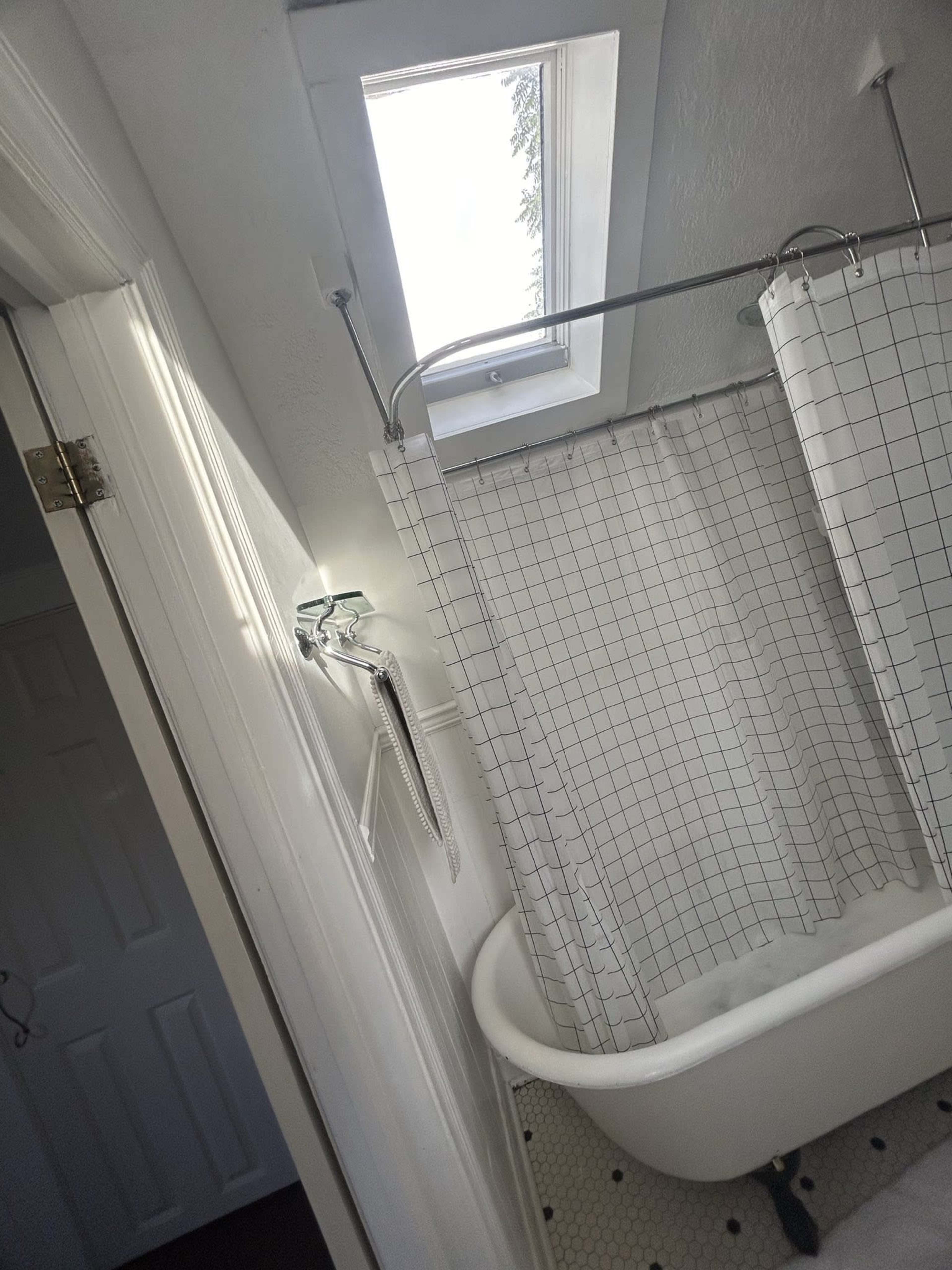 A bathroom with a skylight above a clawfoot bathtub, surrounded by a shower curtain.