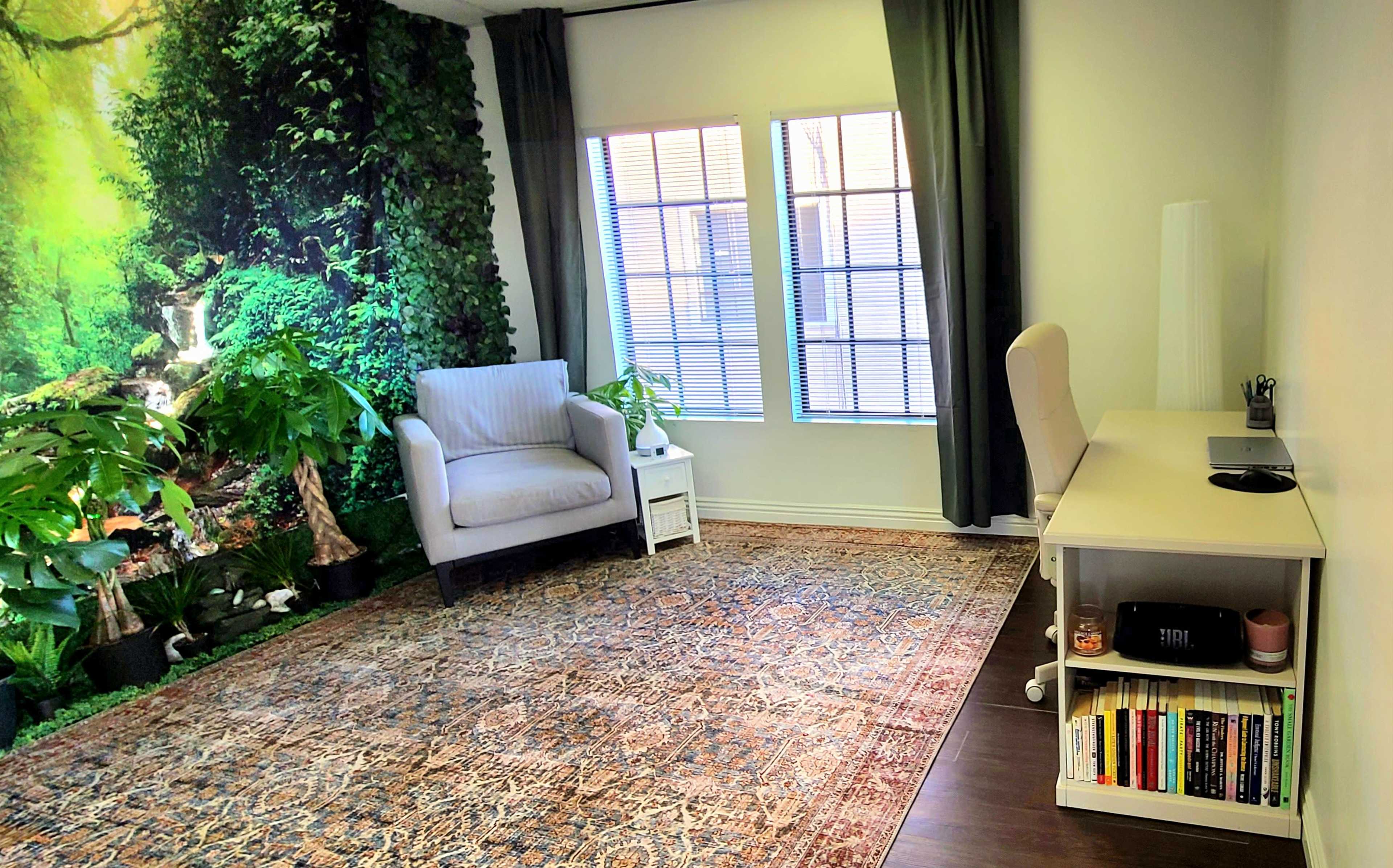 A small, brightly lit room with a chair, desk, and plants, featuring a mural of a forest on one wall.