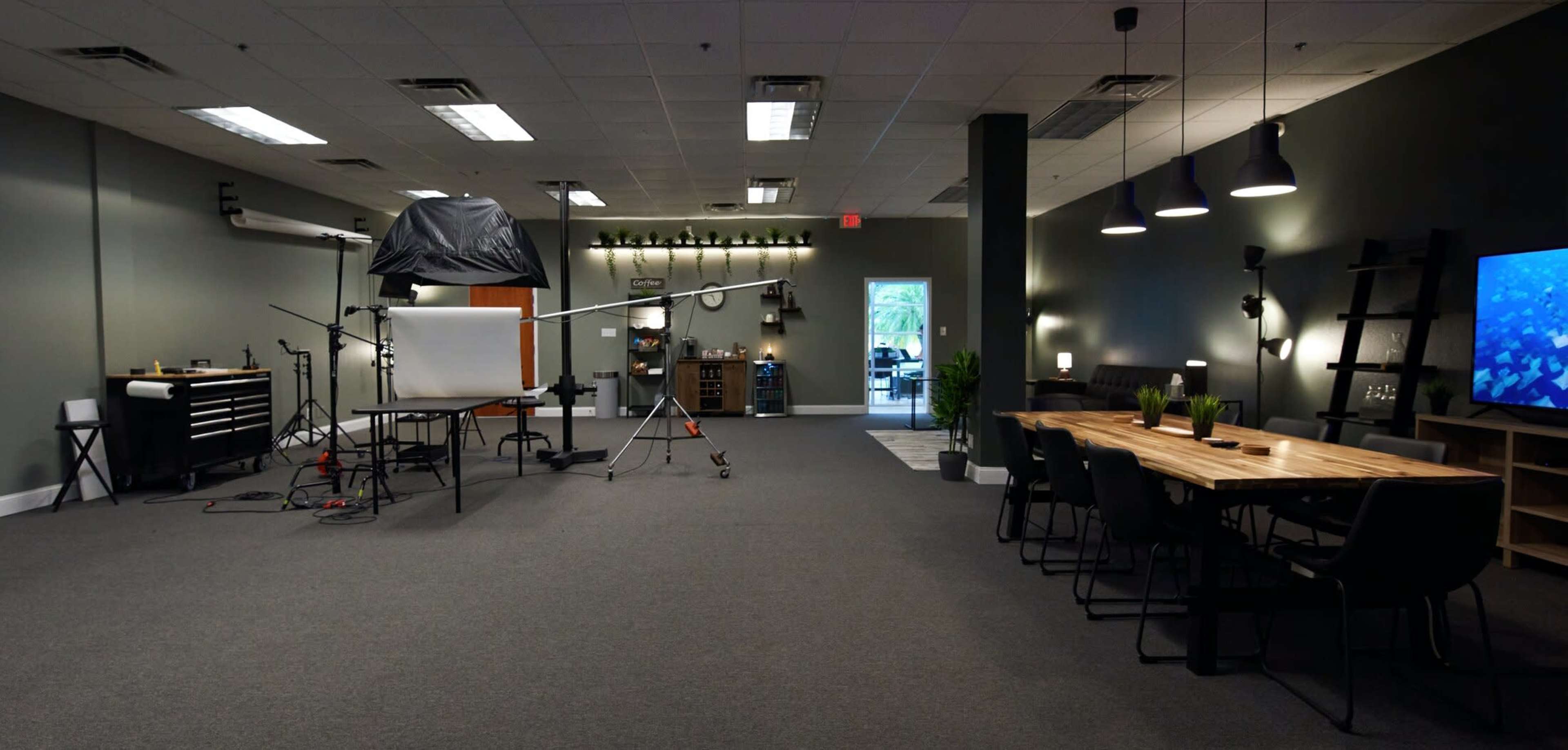 The image shows a spacious studio with a photography setup on one side and a dining area with a long wooden table and chairs on the other.