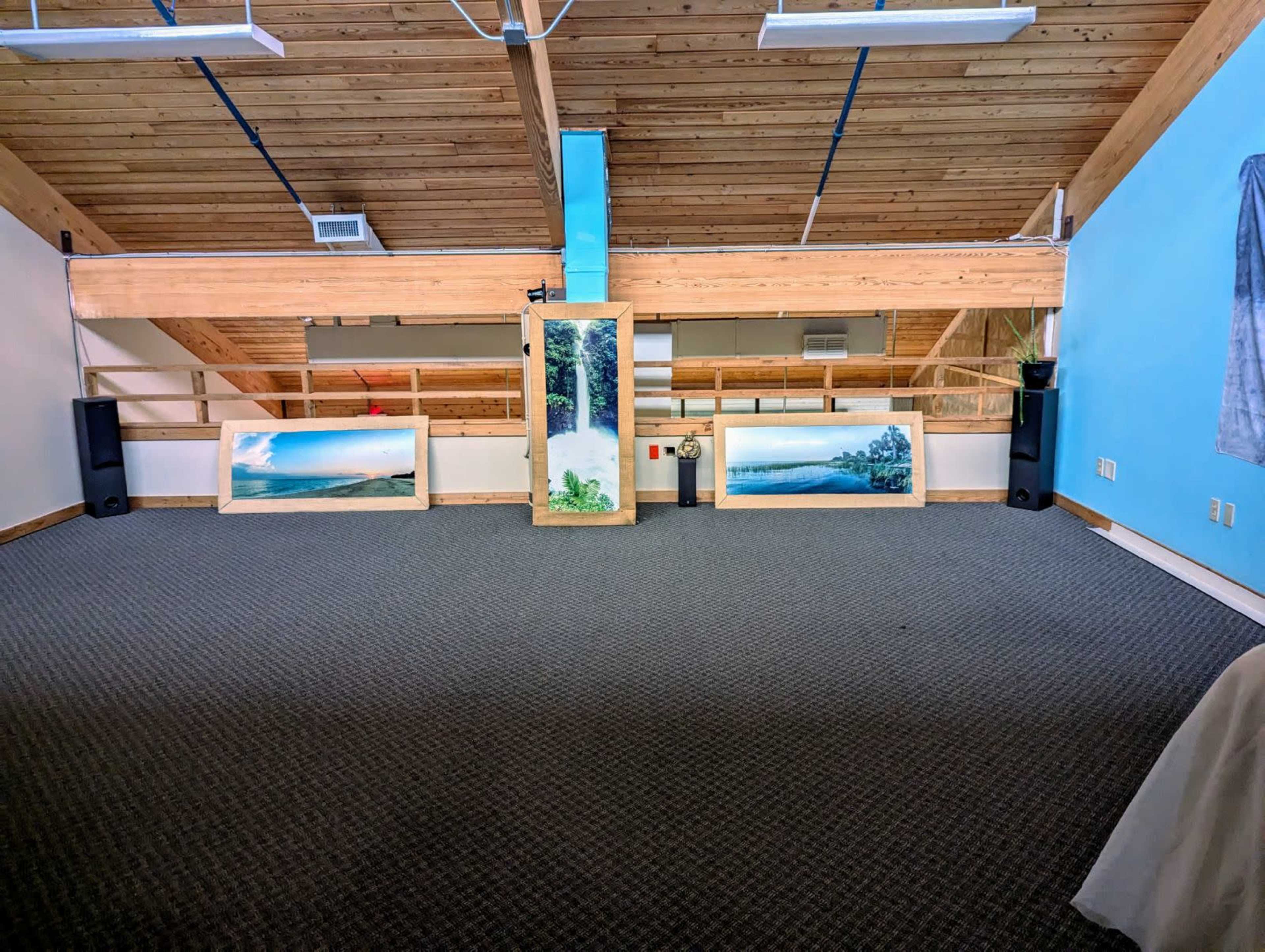 The image shows a spacious room with wooden ceilings, featuring several large paintings displayed on a raised platform.