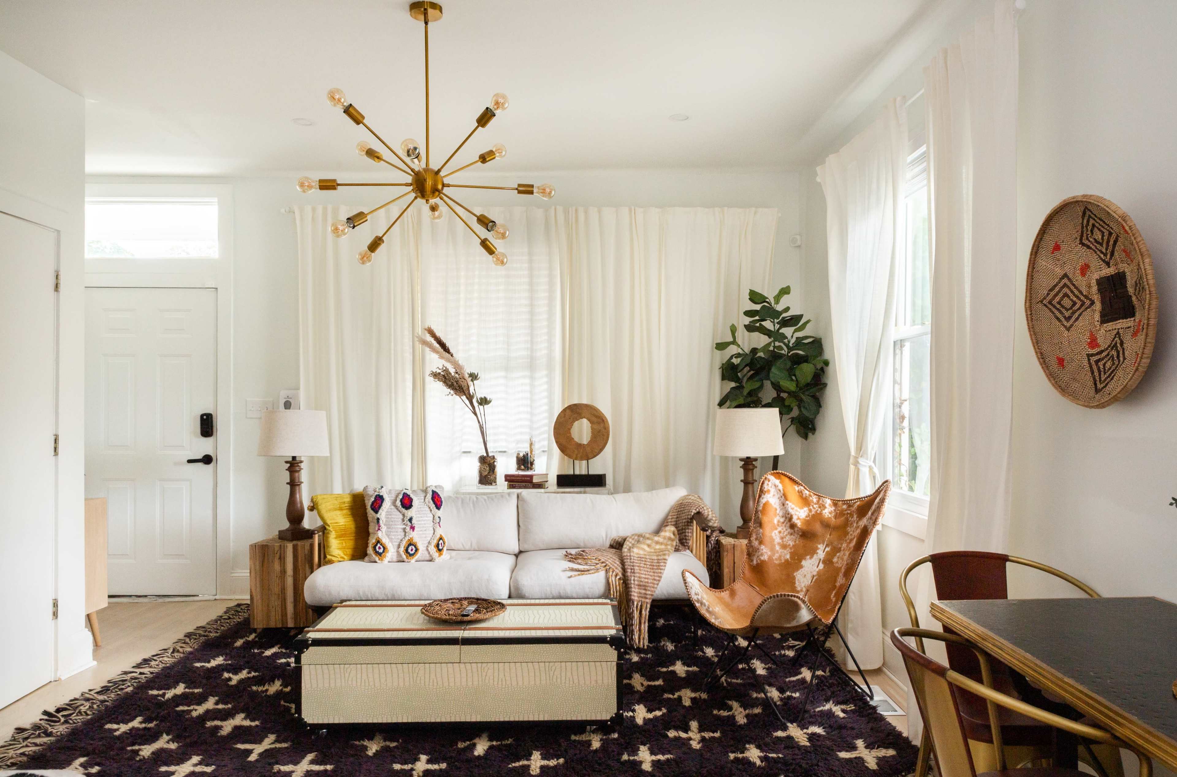 A modern living room features a white sofa, a decorative coffee table, a large black area rug, two lamps, and a leather chair, with potted plants and wall decor enhancing the space.