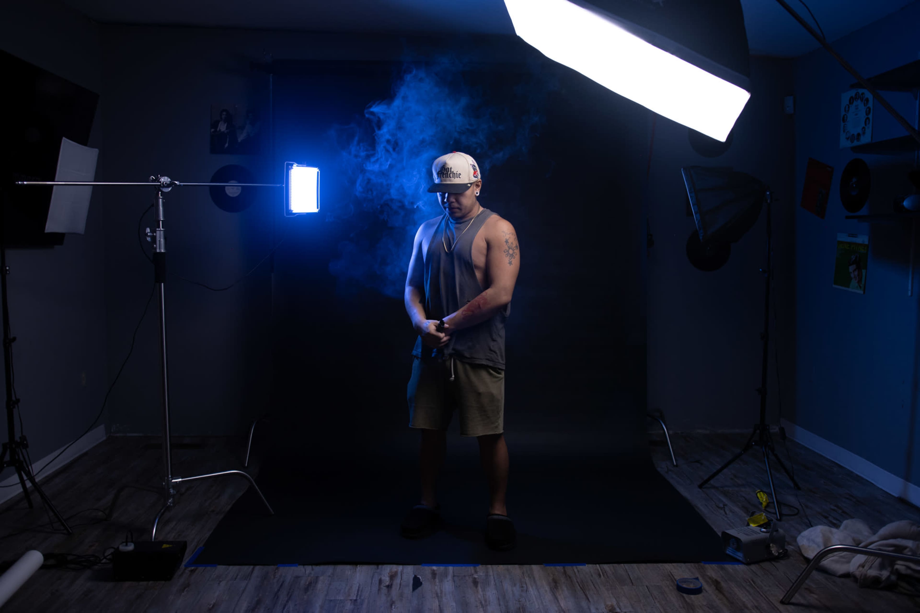 A person stands in a dimly lit studio surrounded by photography equipment and smoke.