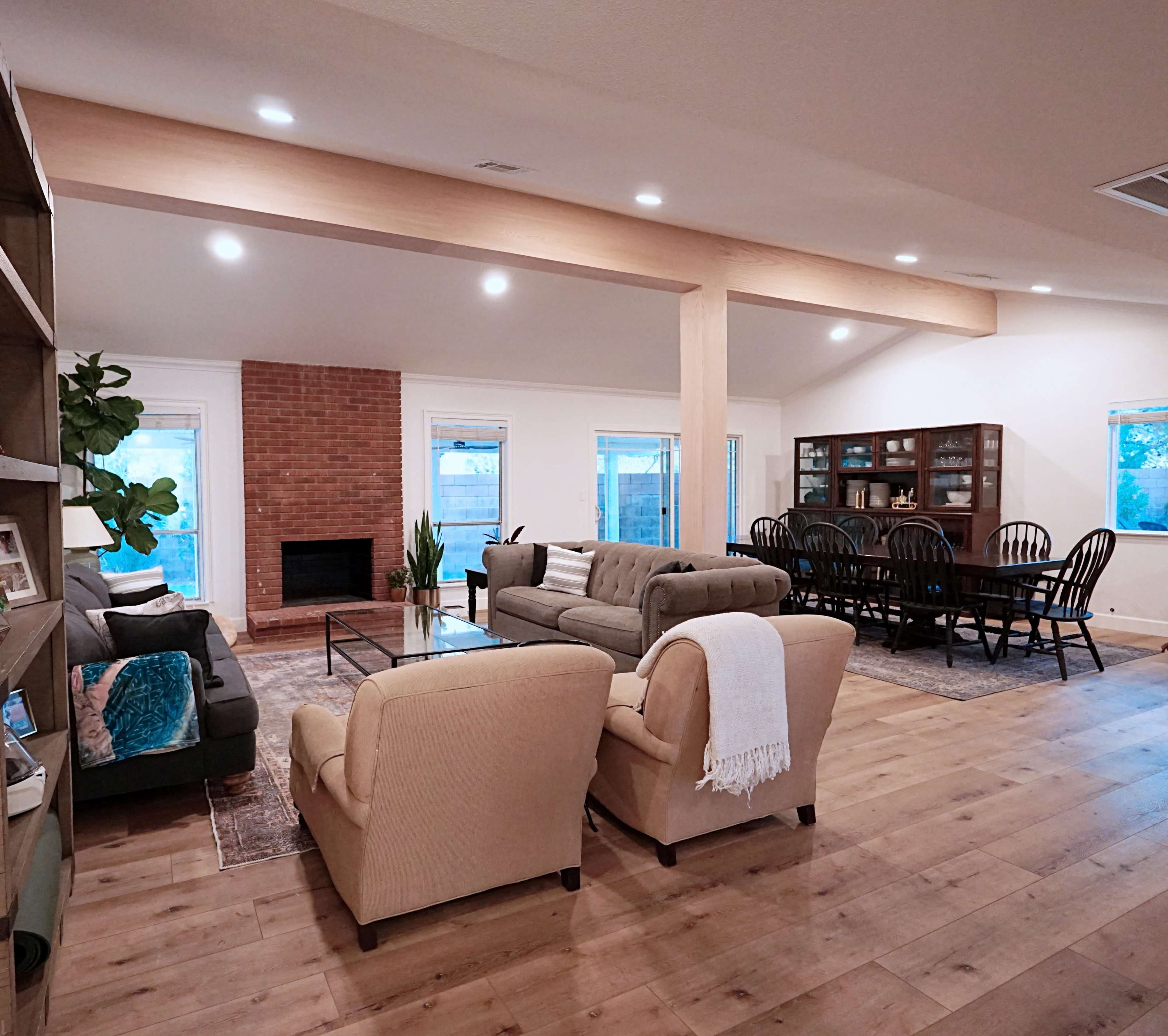 A spacious living area with a seating arrangement, a dining table, a brick fireplace, and large windows letting in natural light.