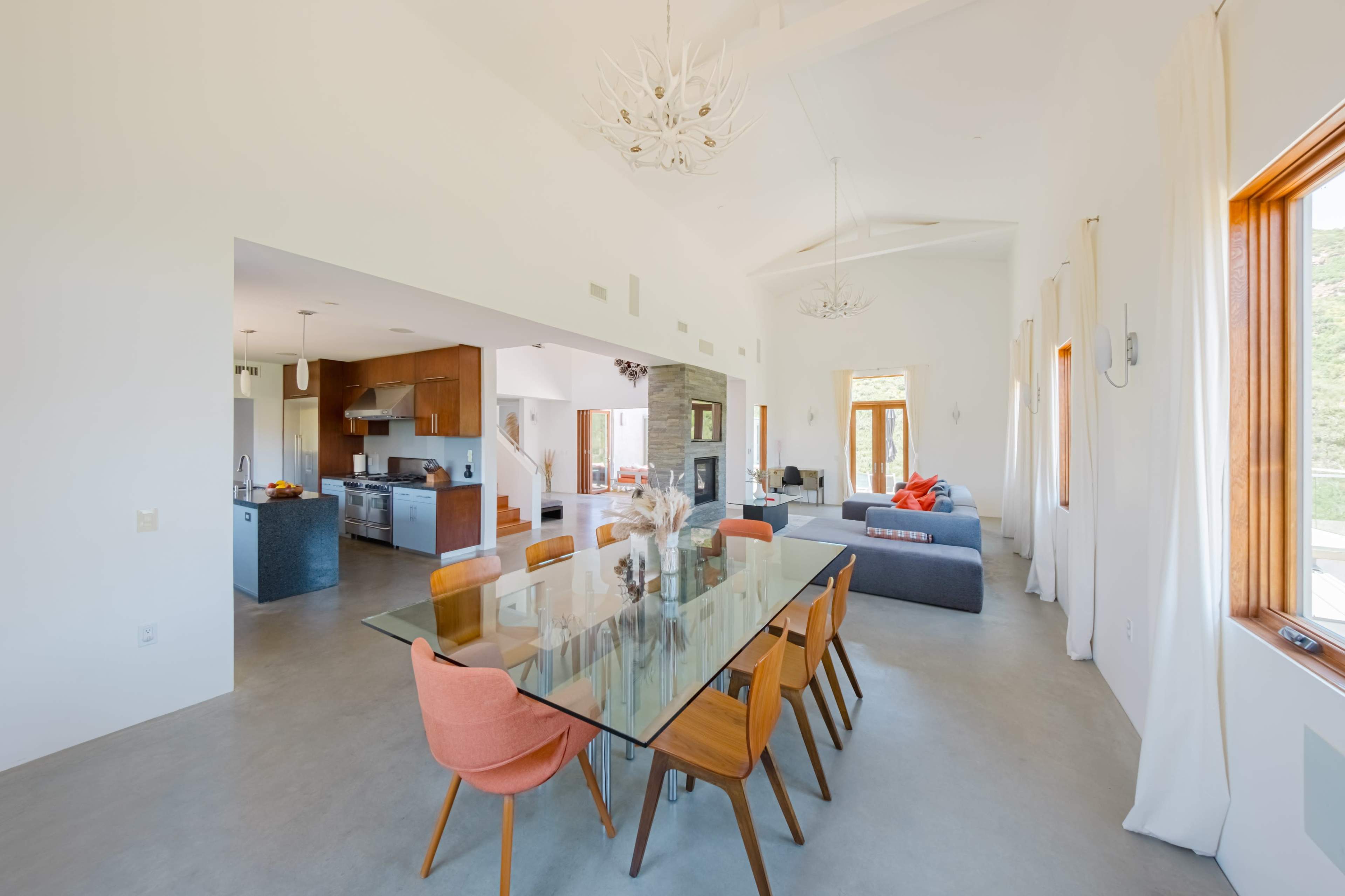 An open-plan living and dining area featuring a glass dining table with wooden chairs, a modern kitchen with stainless steel appliances, and a cozy seating area.