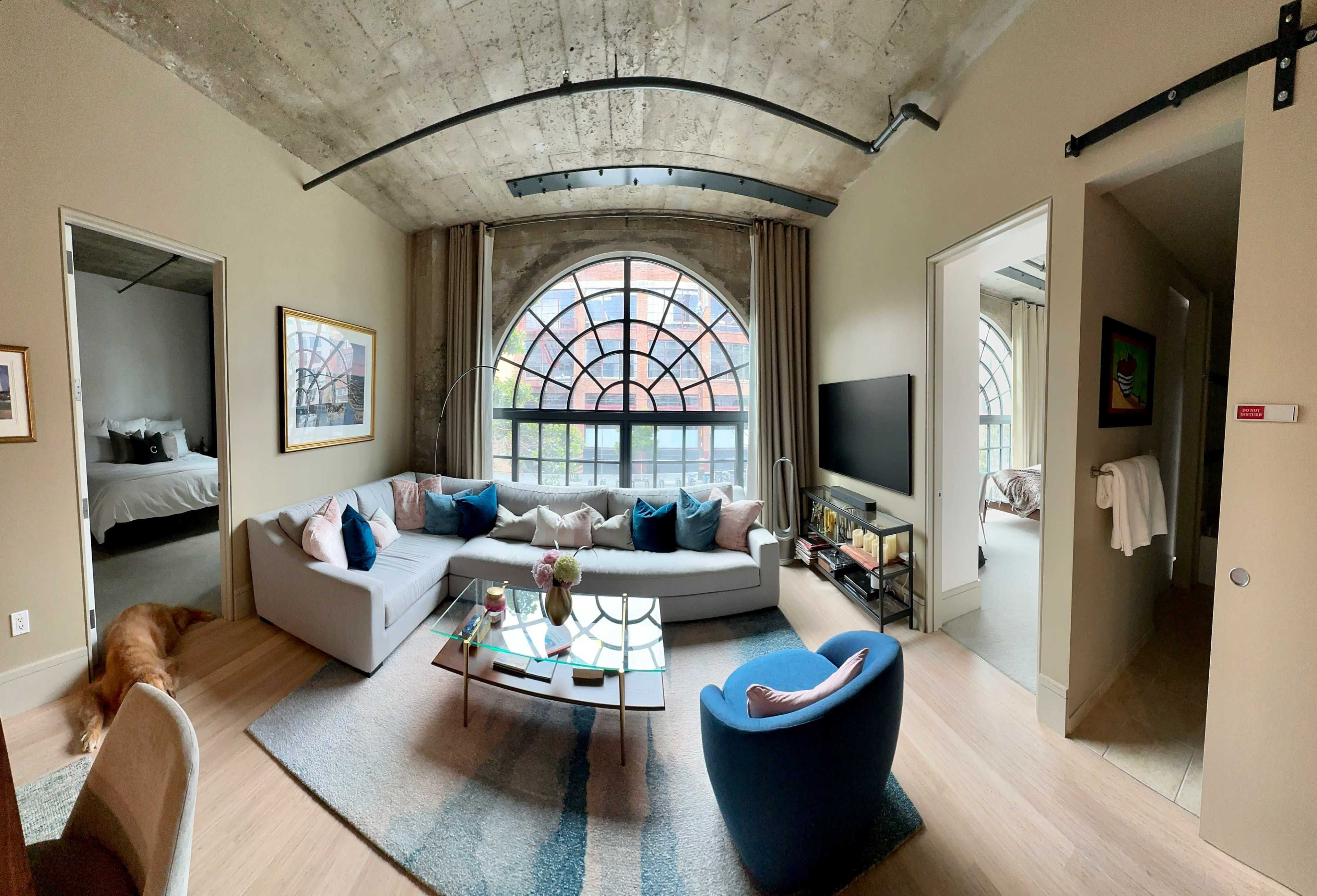 A modern living room with a large arched window, a sectional sofa, a glass coffee table, and a blue armchair.