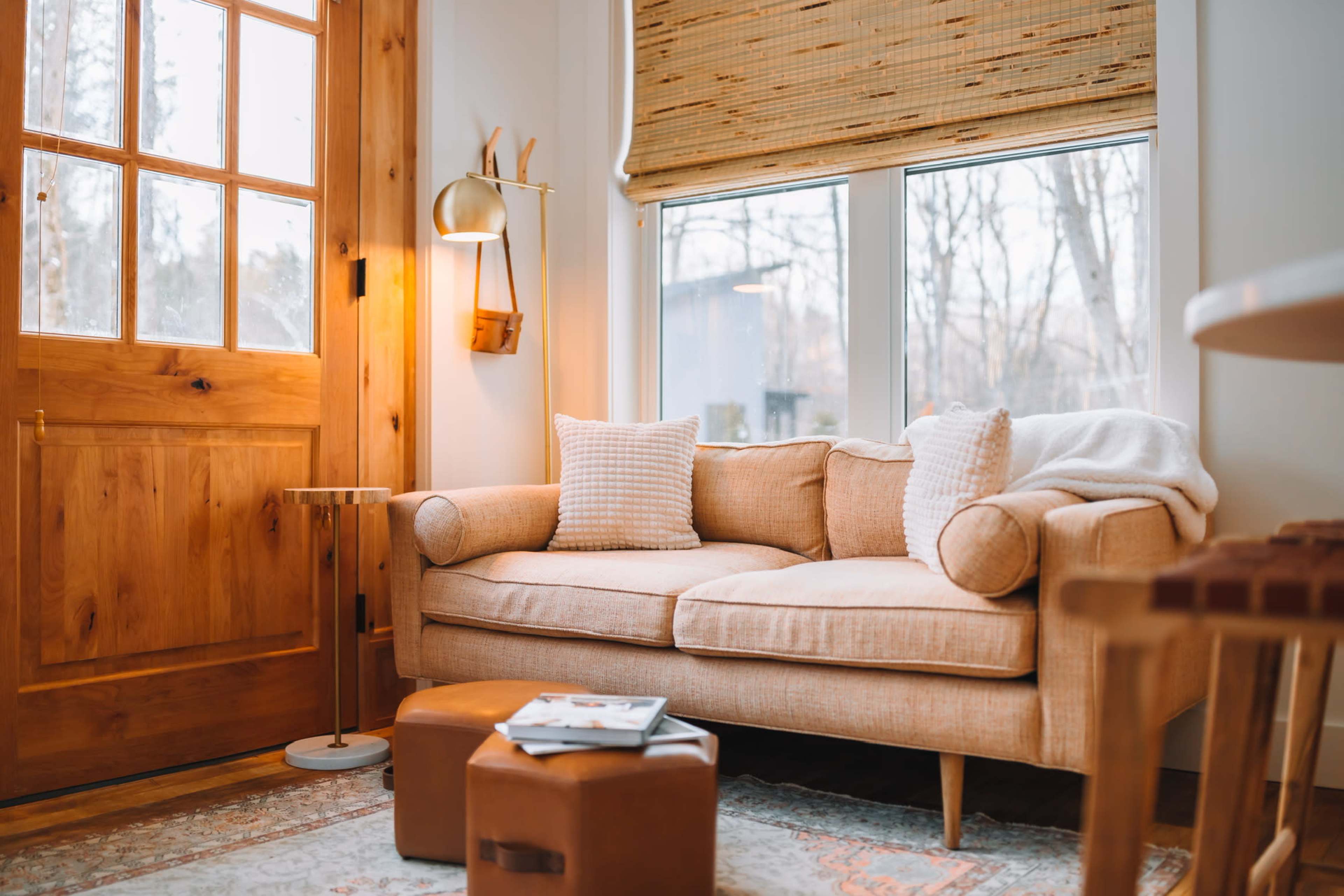 A light-filled room features a cozy beige sofa, large windows, and wooden flooring.
