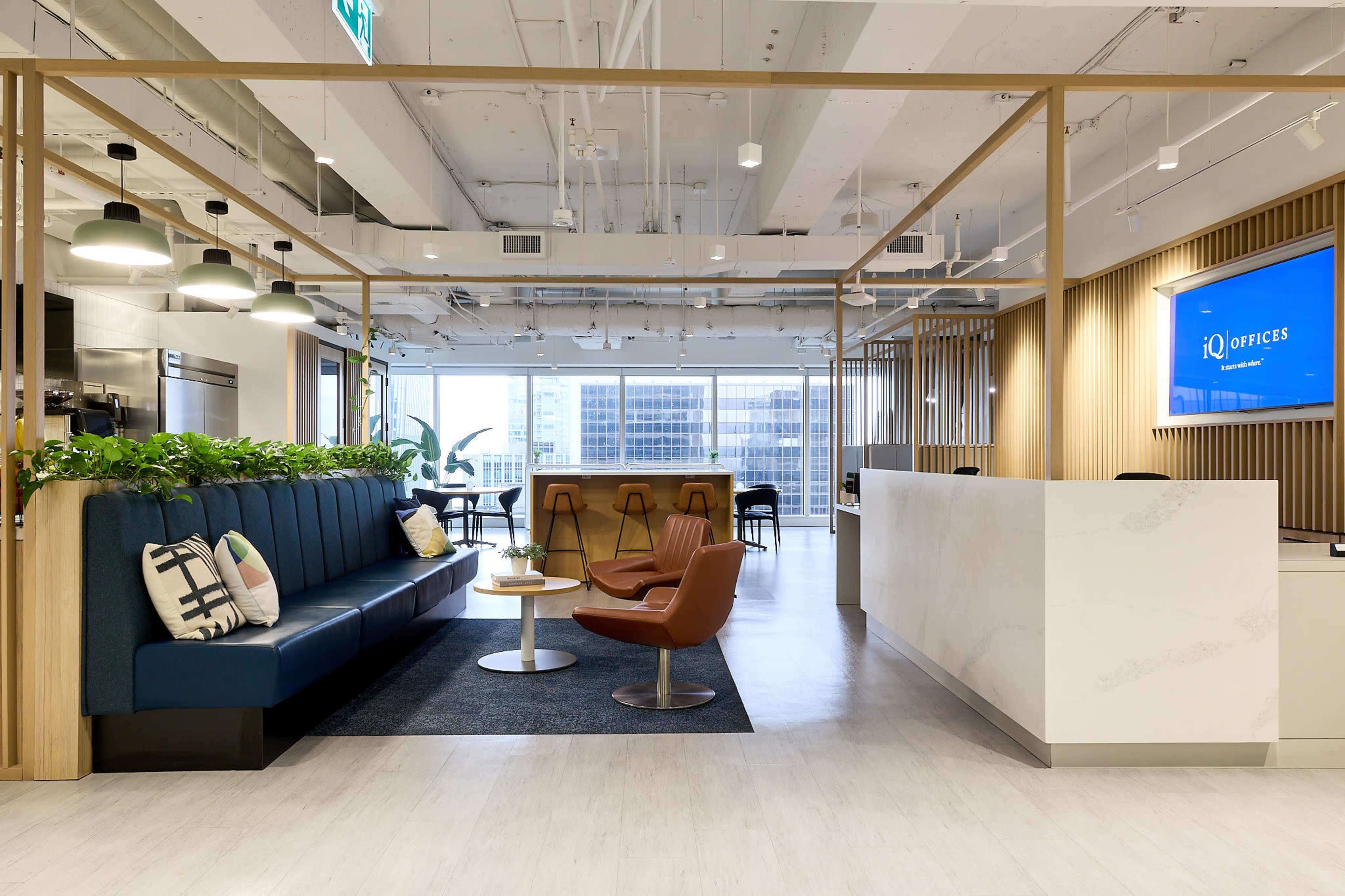 The image shows a modern office reception area featuring a blue sofa, wooden accents, and large windows with city views.