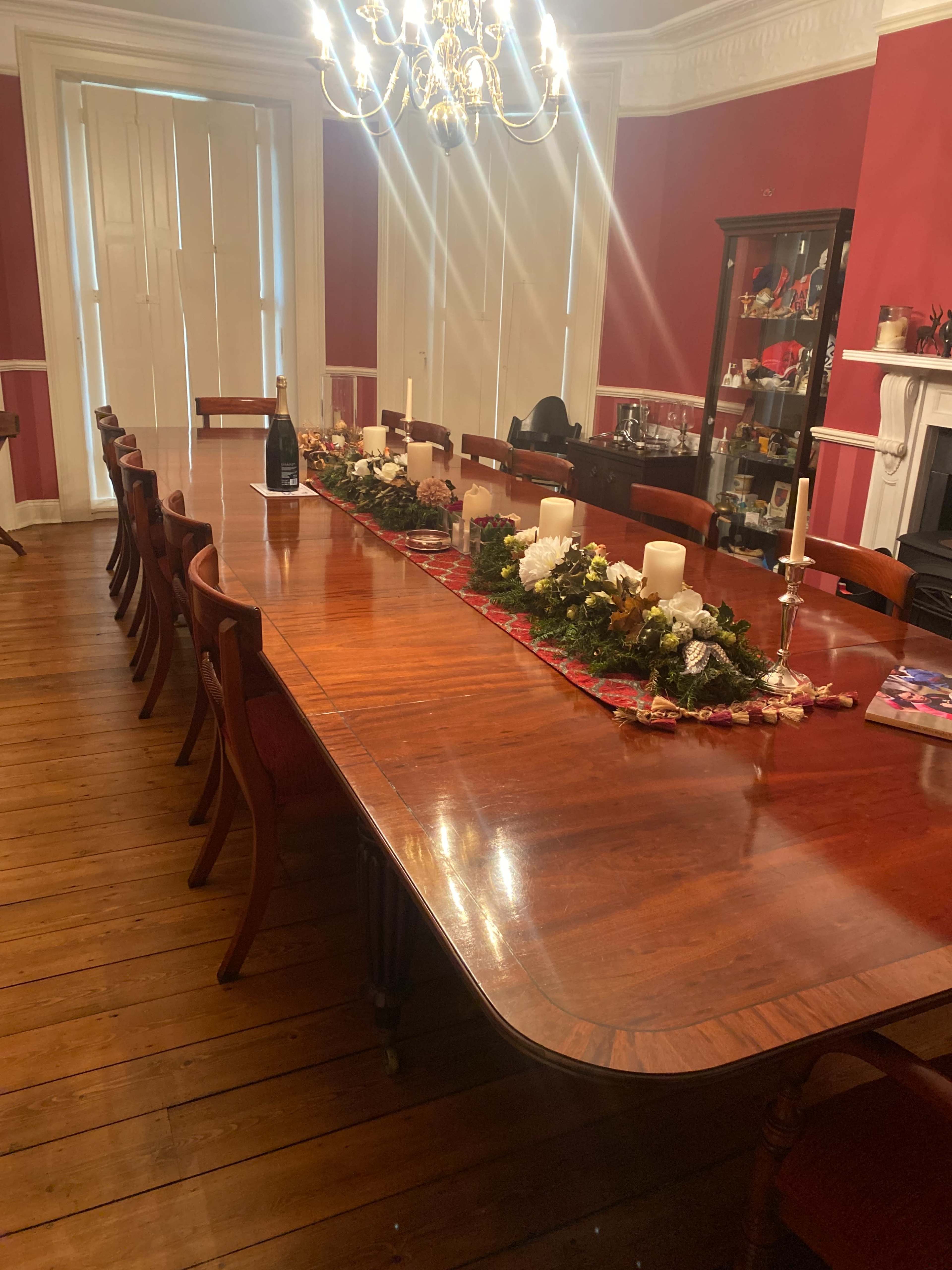 A long wooden dining table is set in a red-walled room, decorated with a festive centerpiece and surrounded by chairs.