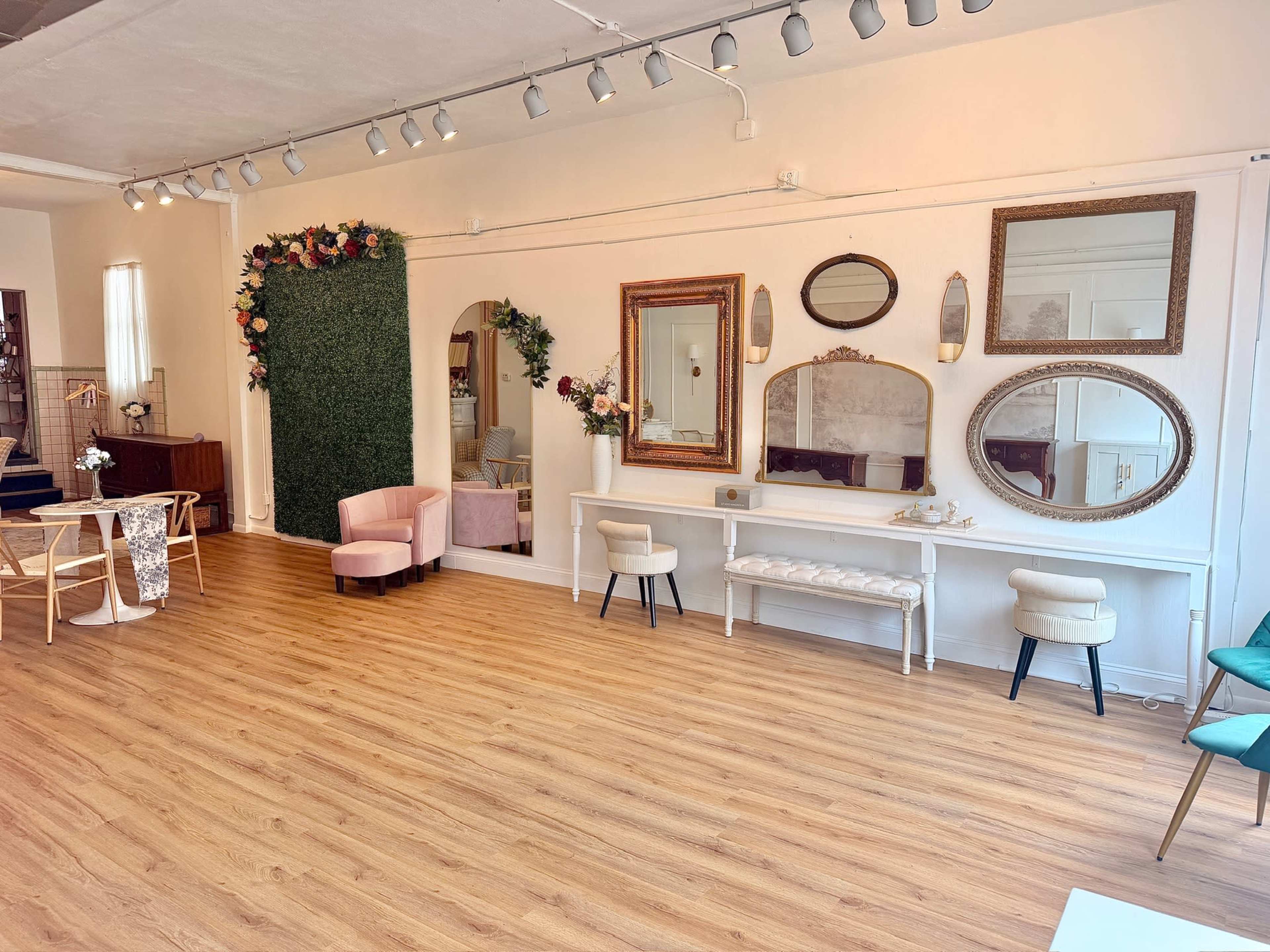 The image shows a brightly lit, spacious room with wooden flooring, decorated with mirrors, a green wall, and various seating arrangements.