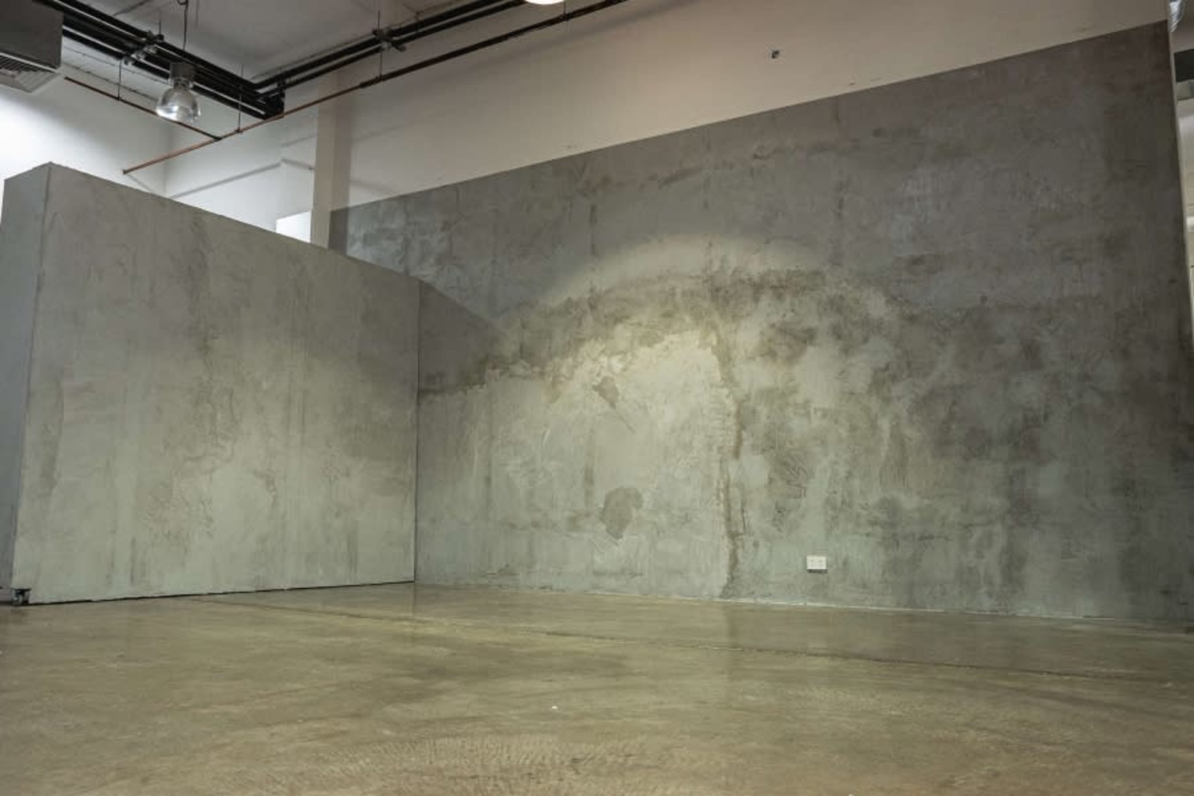 An empty interior space with two large concrete walls and a polished concrete floor.