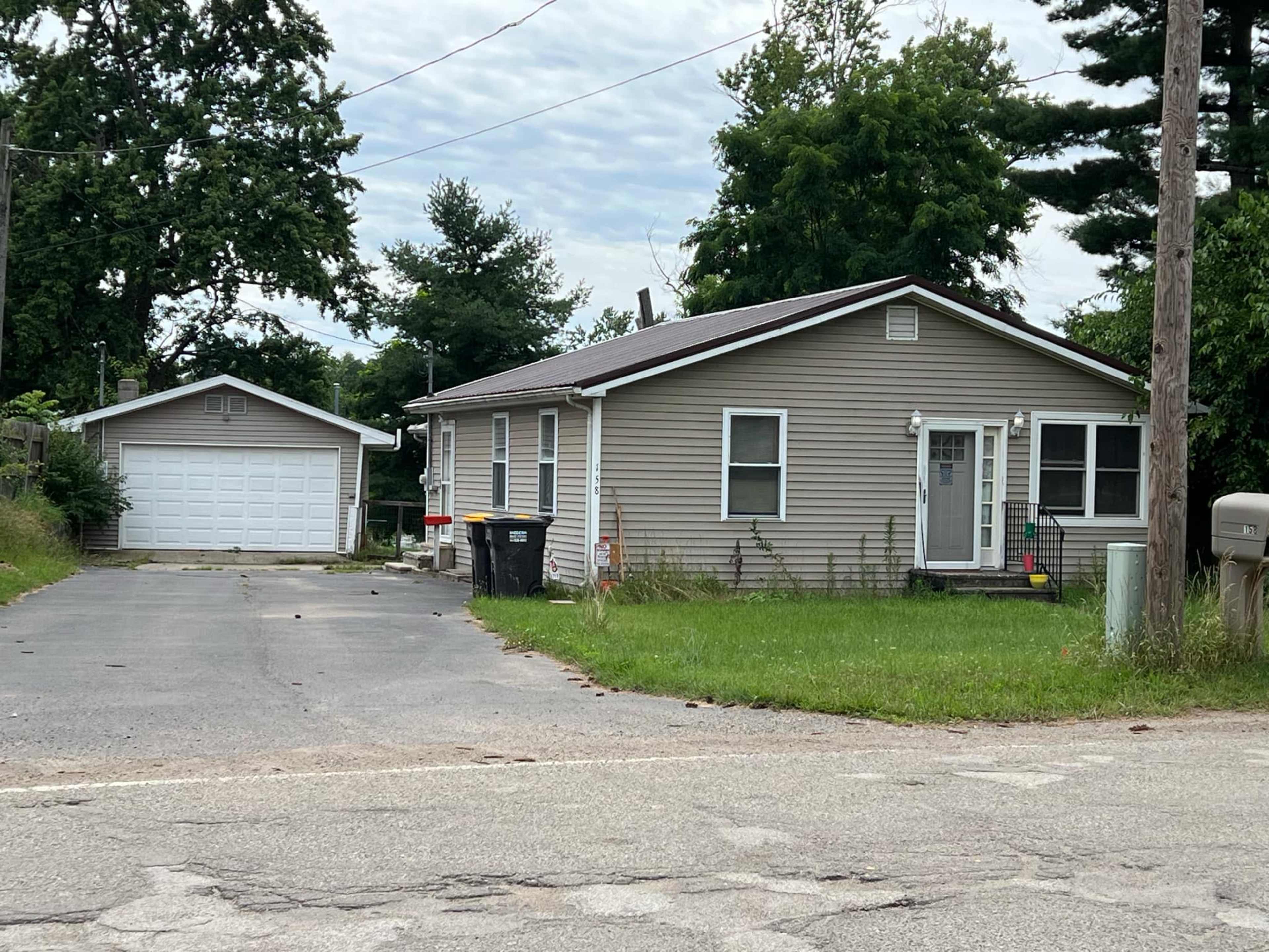 The image shows a single-story house with a garage, located on a gravel driveway beside a road.