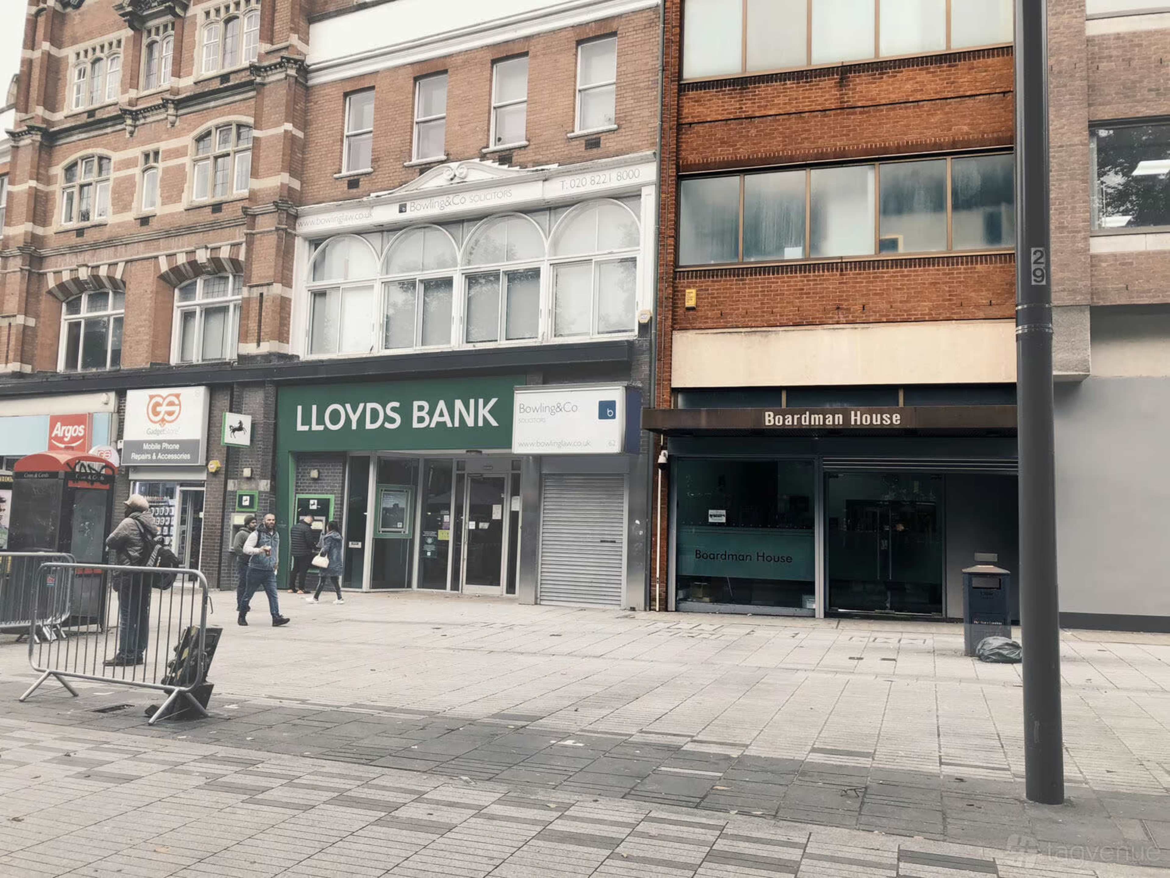 The image shows a street scene with several commercial buildings, including a Lloyds Bank and Boardman House, along with a few pedestrians and barriers on the sidewalk.