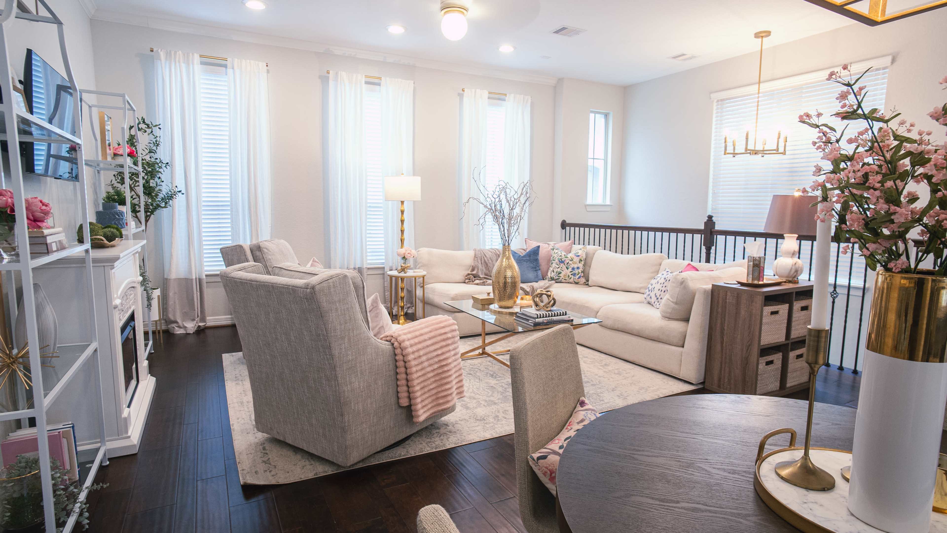 A light-filled living room features a beige sectional sofa, a glass coffee table, and decorative accents on a dark wood floor.