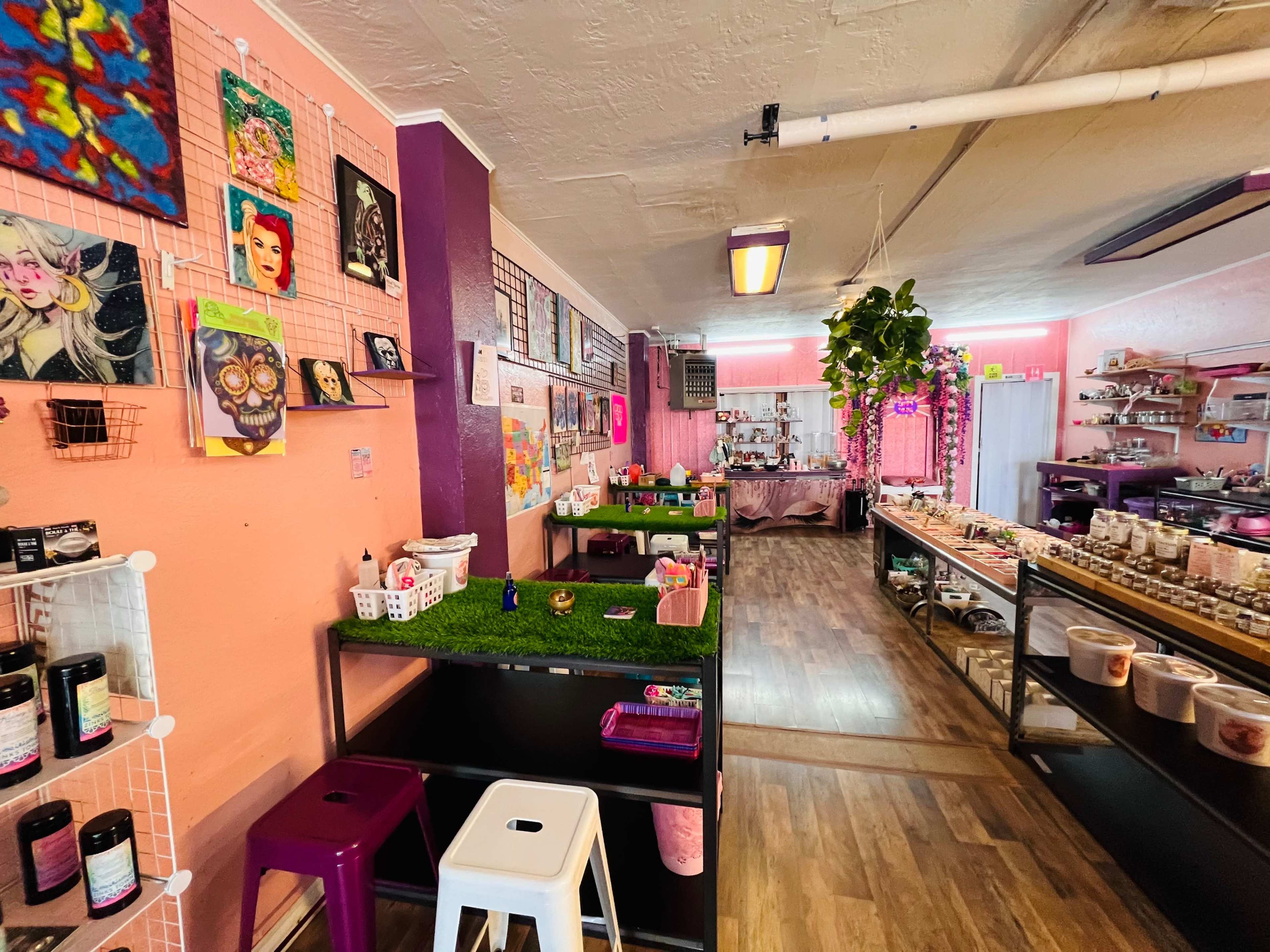 An artsy shop interior with display tables featuring colorful artworks, candles, and decorative items against pastel walls.