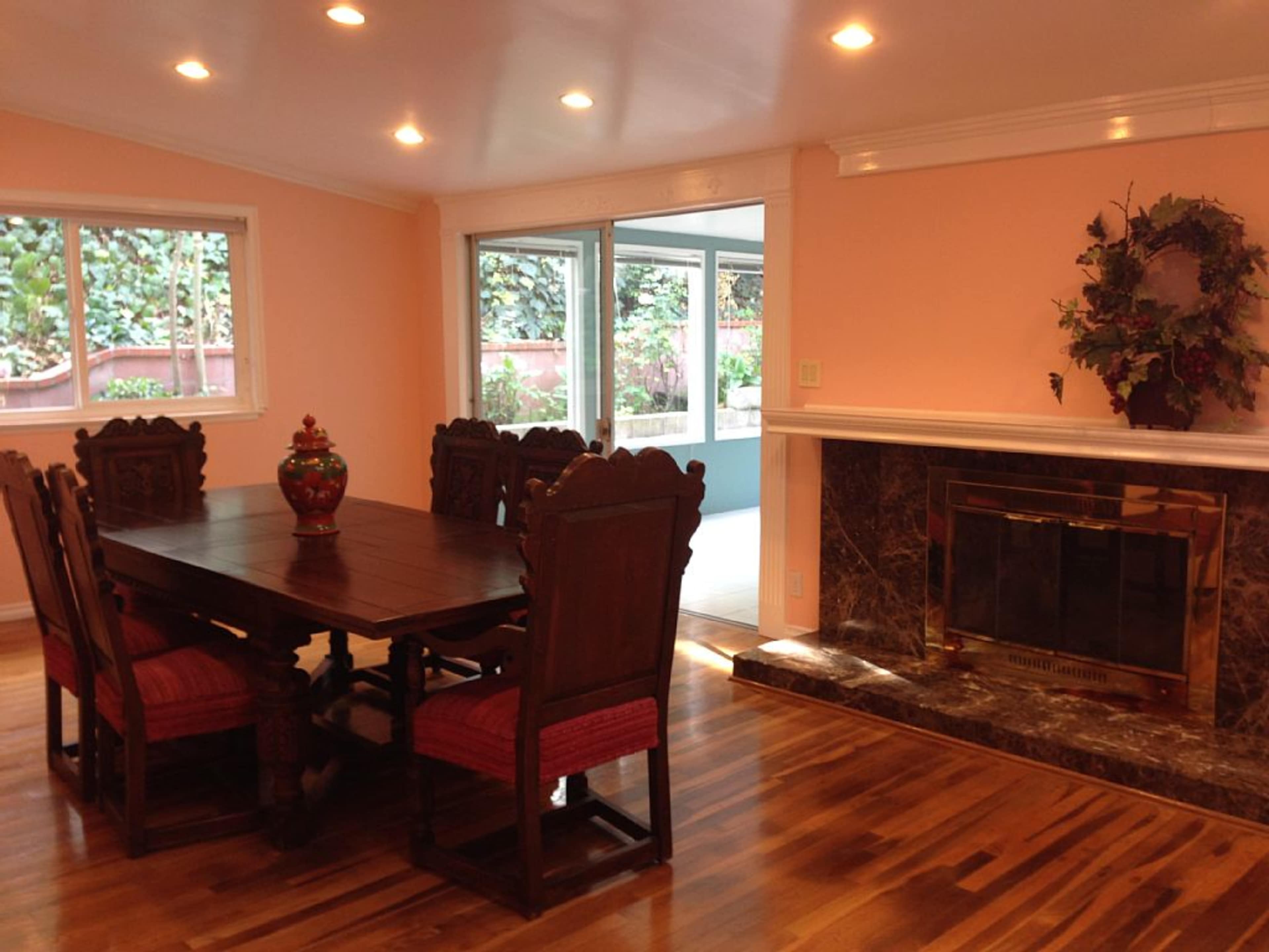 A dining area with a large wooden table and chairs, a decorative vase in the center, and a fireplace against a peach-colored wall.