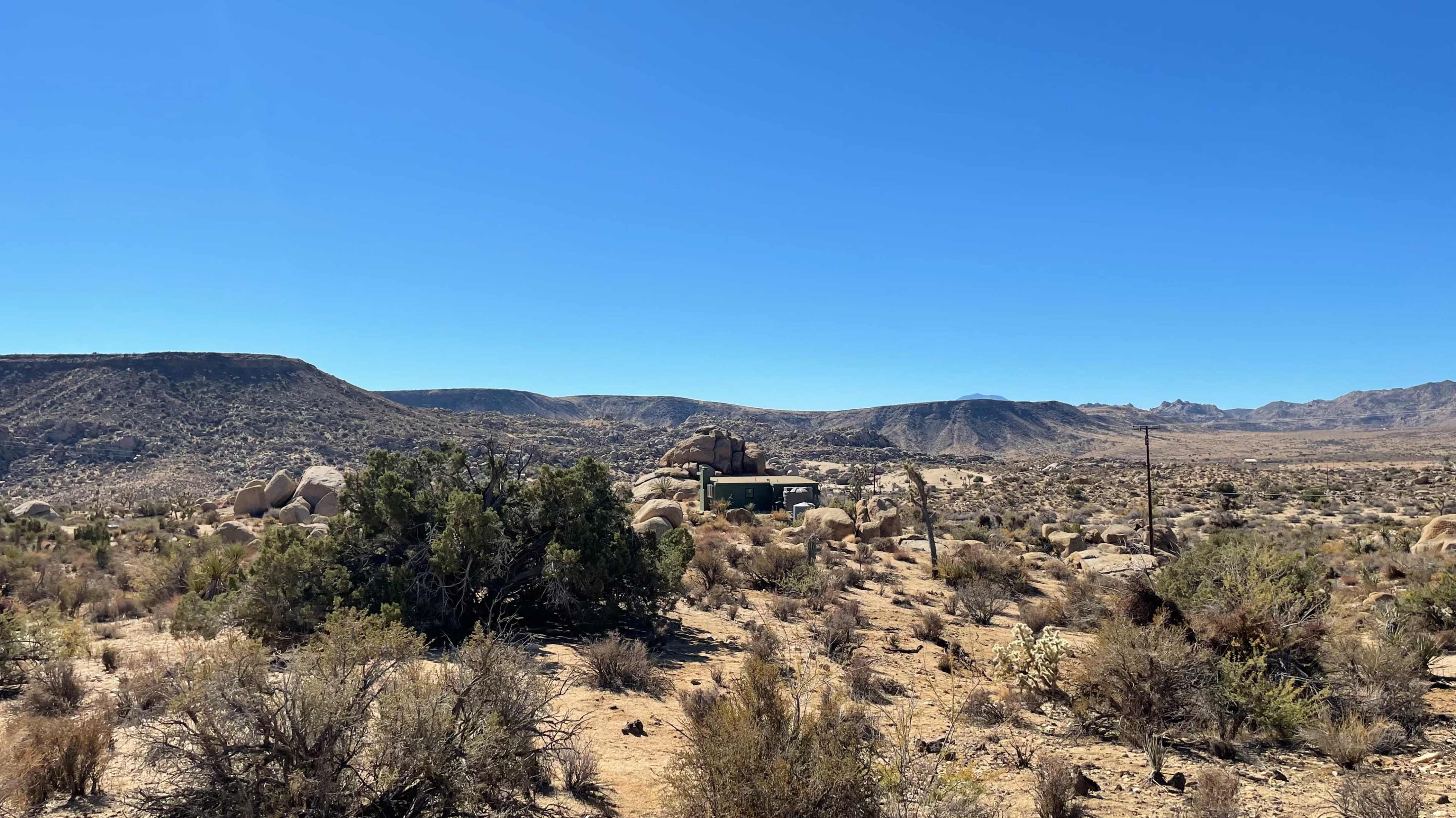 A small green structure is situated among rocky terrain and sparse vegetation in a desert landscape.