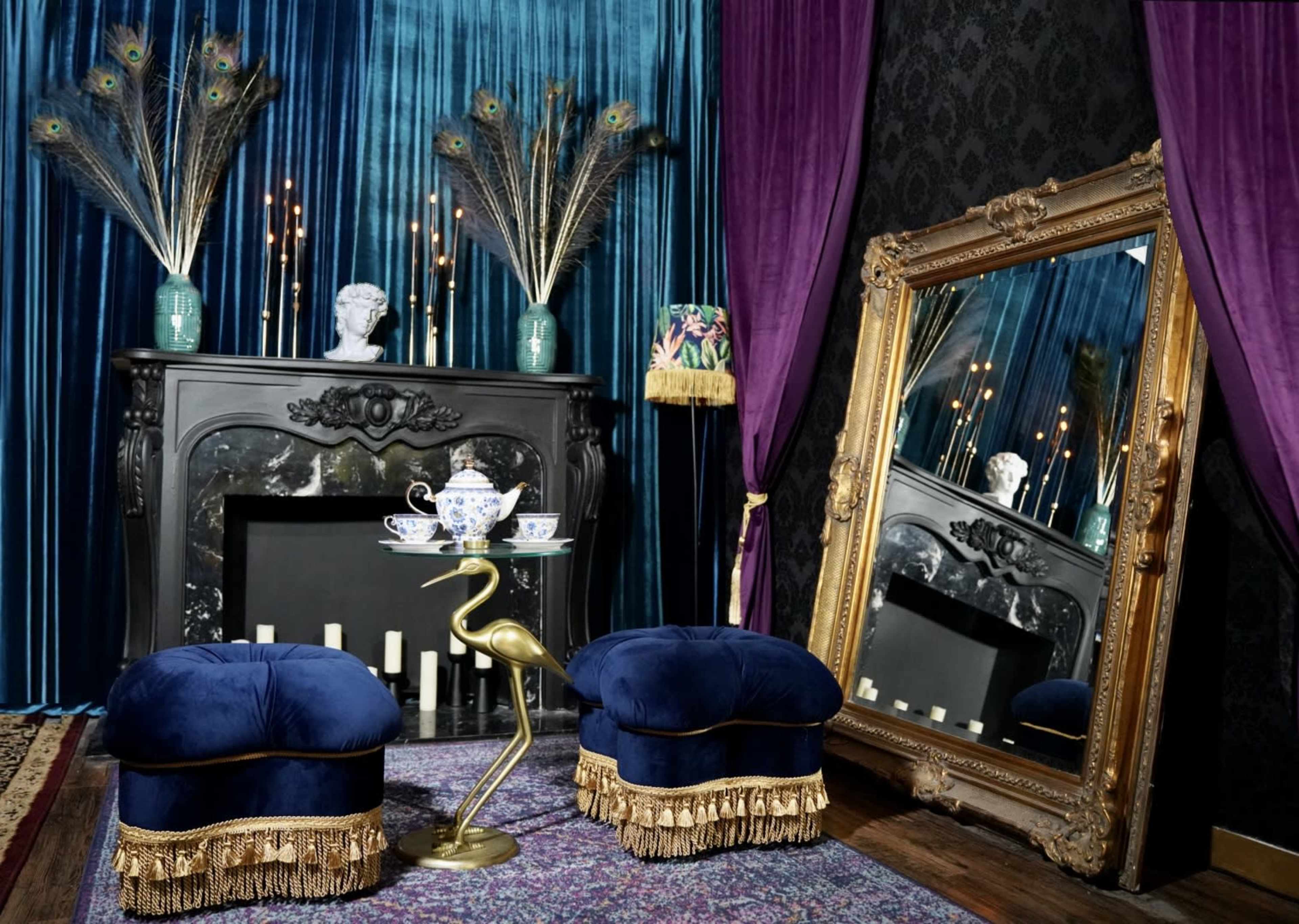 An elegant interior scene featuring a black fireplace, ornate mirror, and velvet seating with peacock feather decor against a dark, patterned wall.