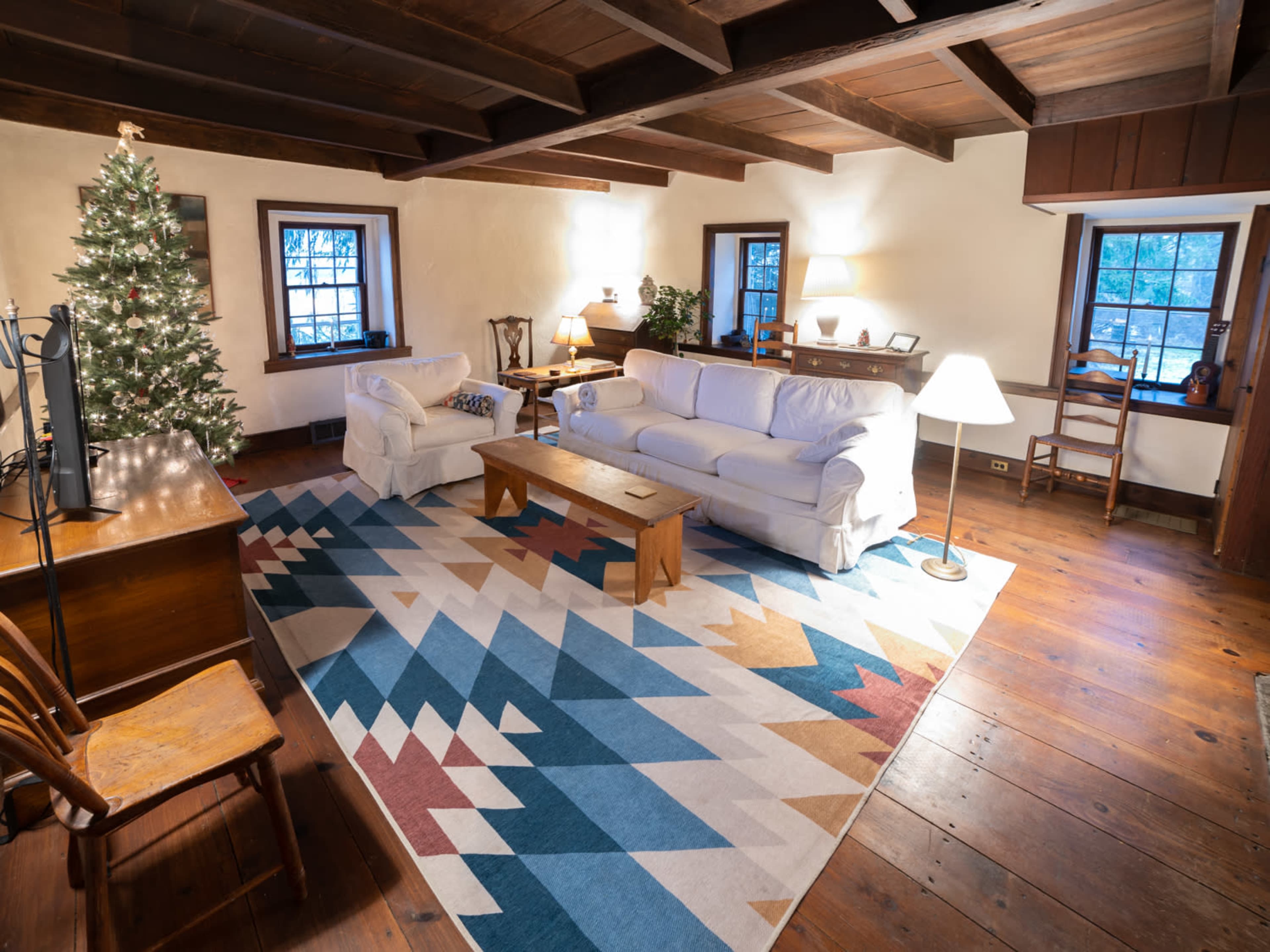 The living room features a Christmas tree, a white couch, a wooden coffee table, and a colorful area rug on a wooden floor.
