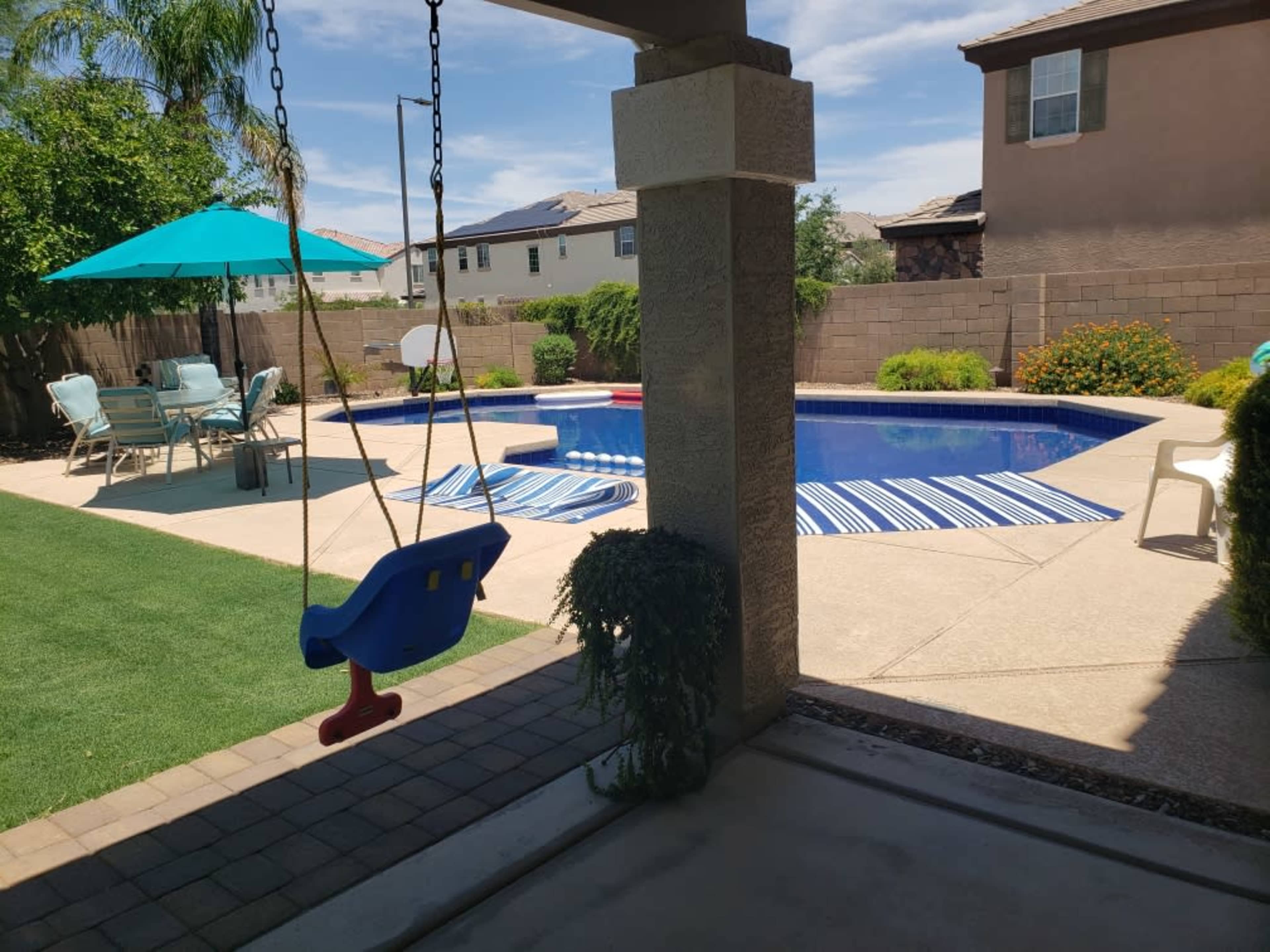 A backyard features a swing, swimming pool, lounge chairs, and an umbrella.