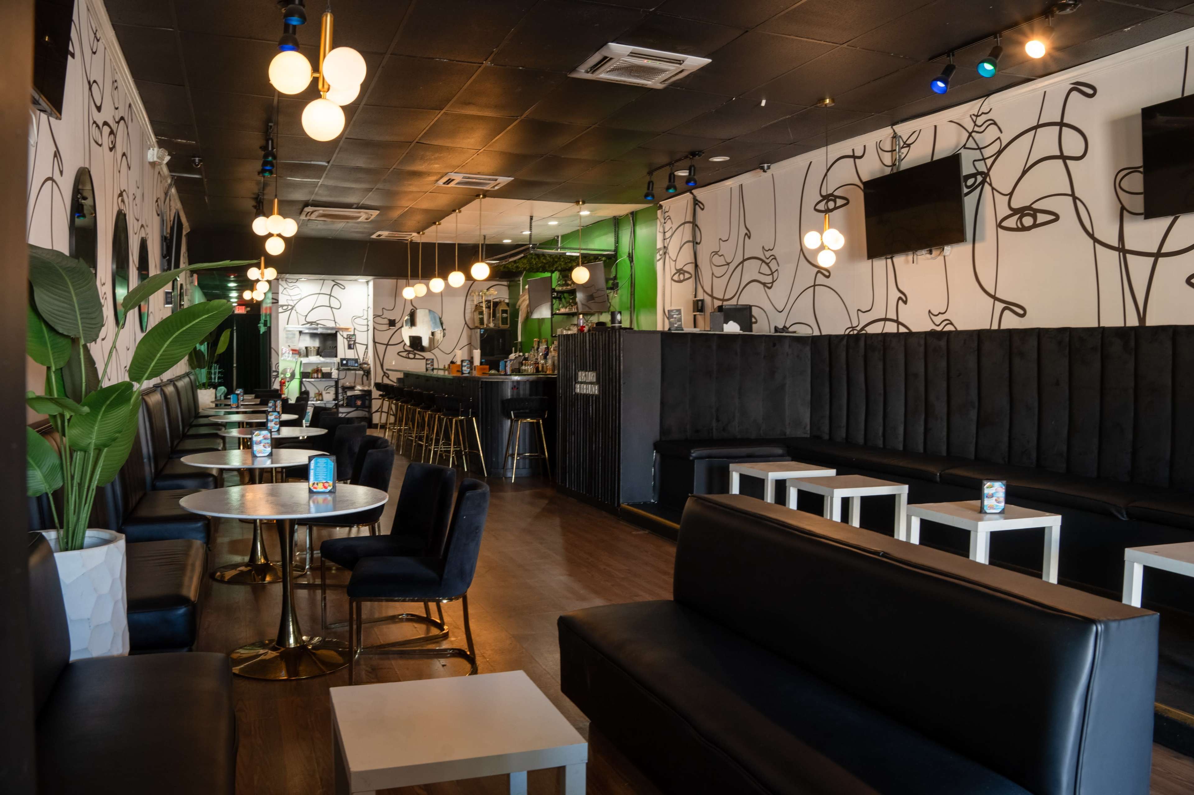 The image shows a modern lounge with black seating, round tables, and minimalist decor featuring wall art and pendant lighting.