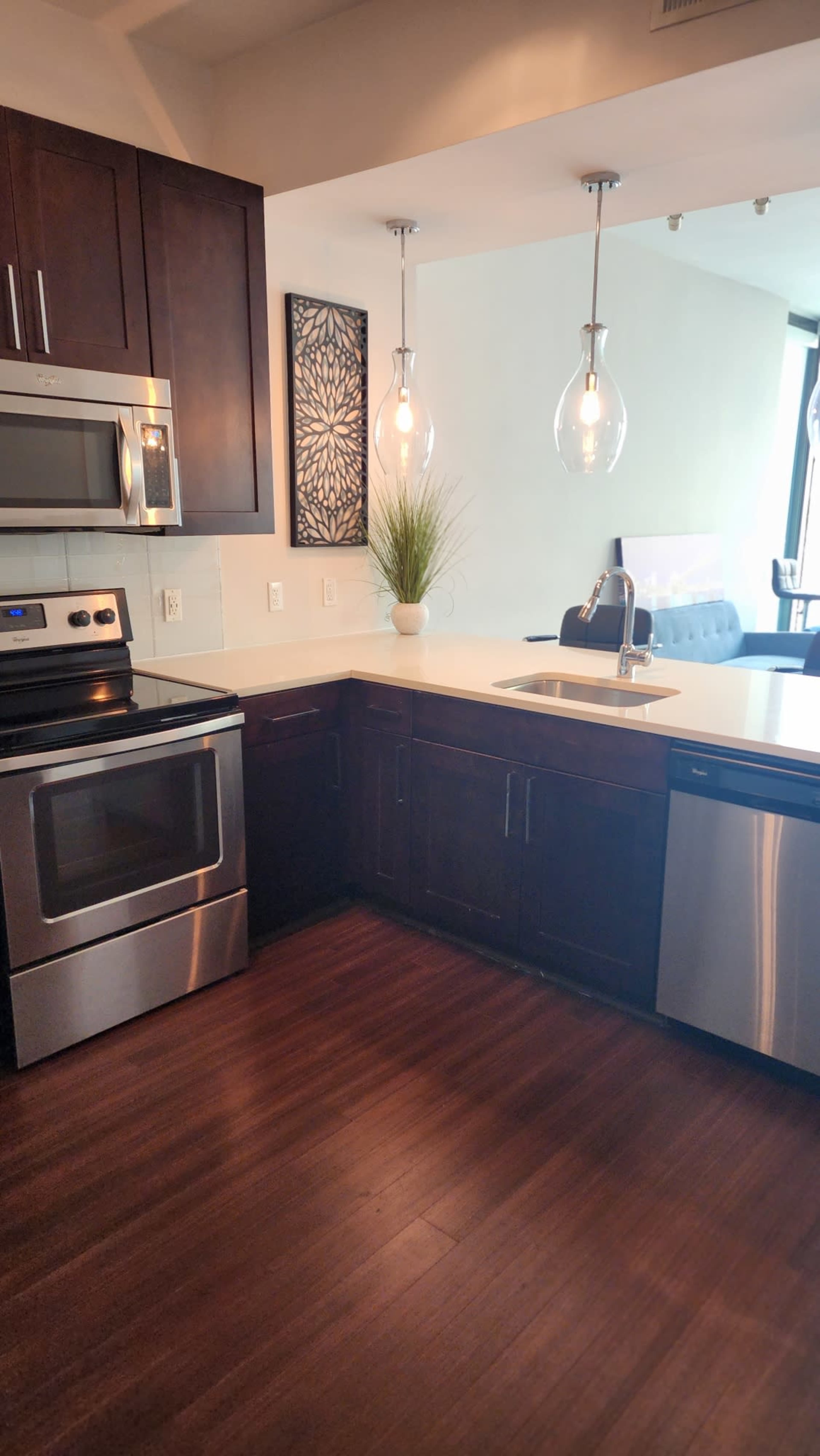 A modern kitchen with dark cabinetry, stainless steel appliances, and pendant lighting over a white countertop.