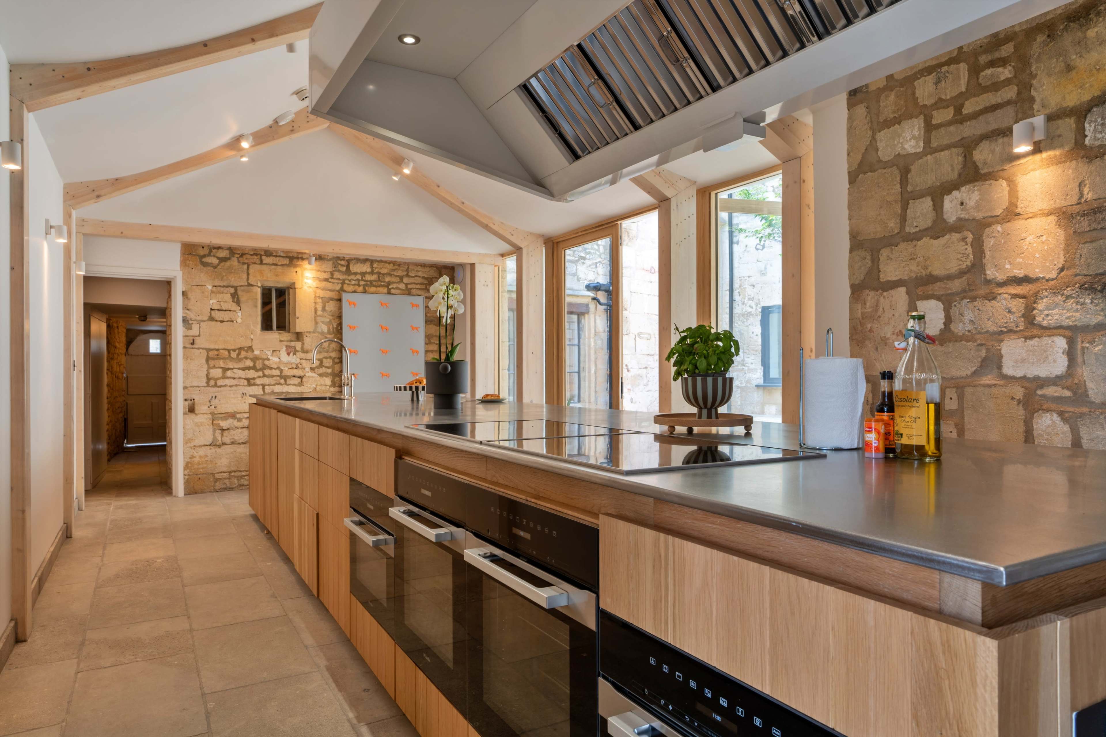 The kitchen features a central island with built-in appliances surrounded by stone walls and large windows that provide natural light.