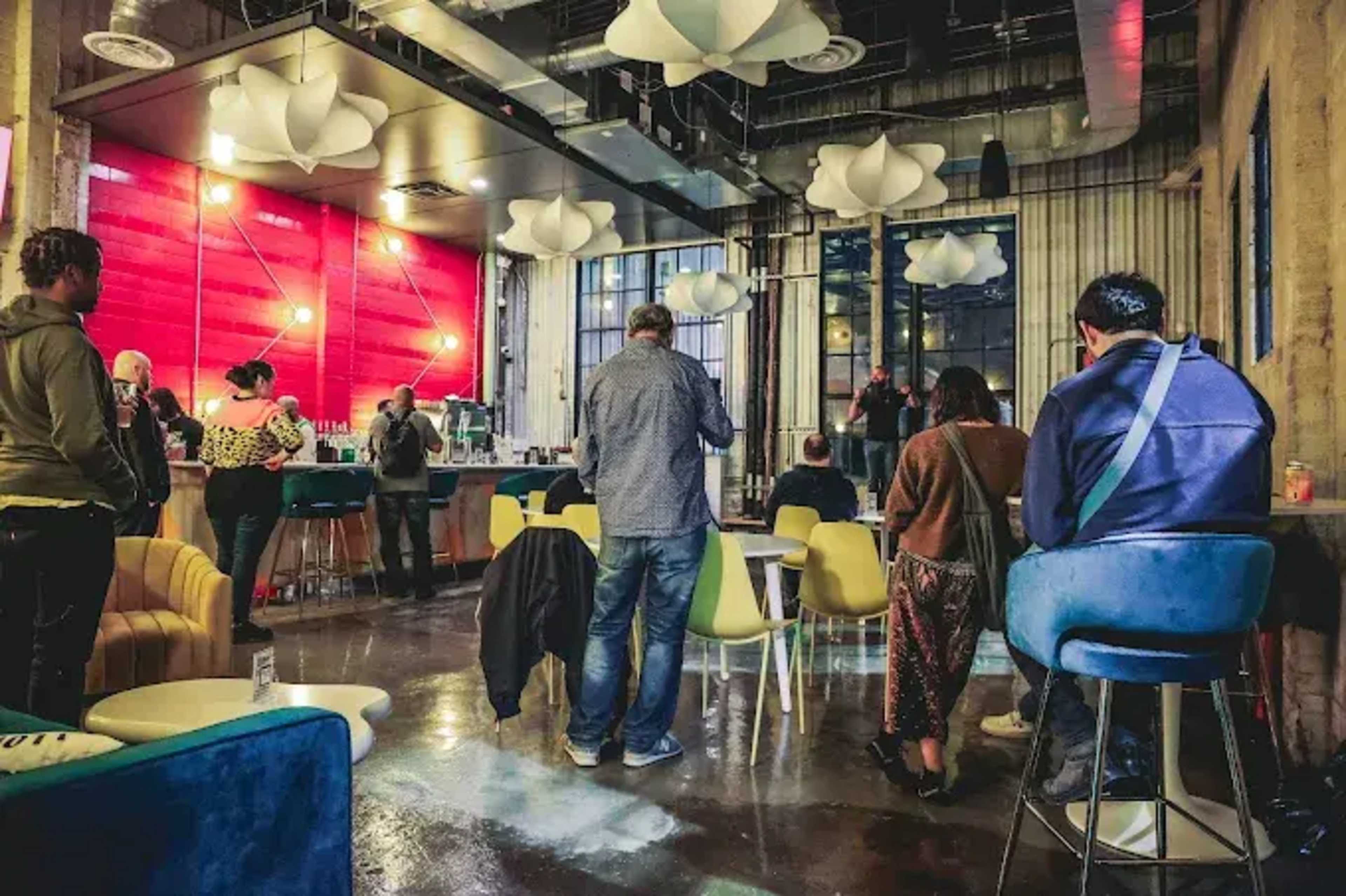 A group of people stands and sits in a modern cafe featuring colorful lighting and contemporary furniture.