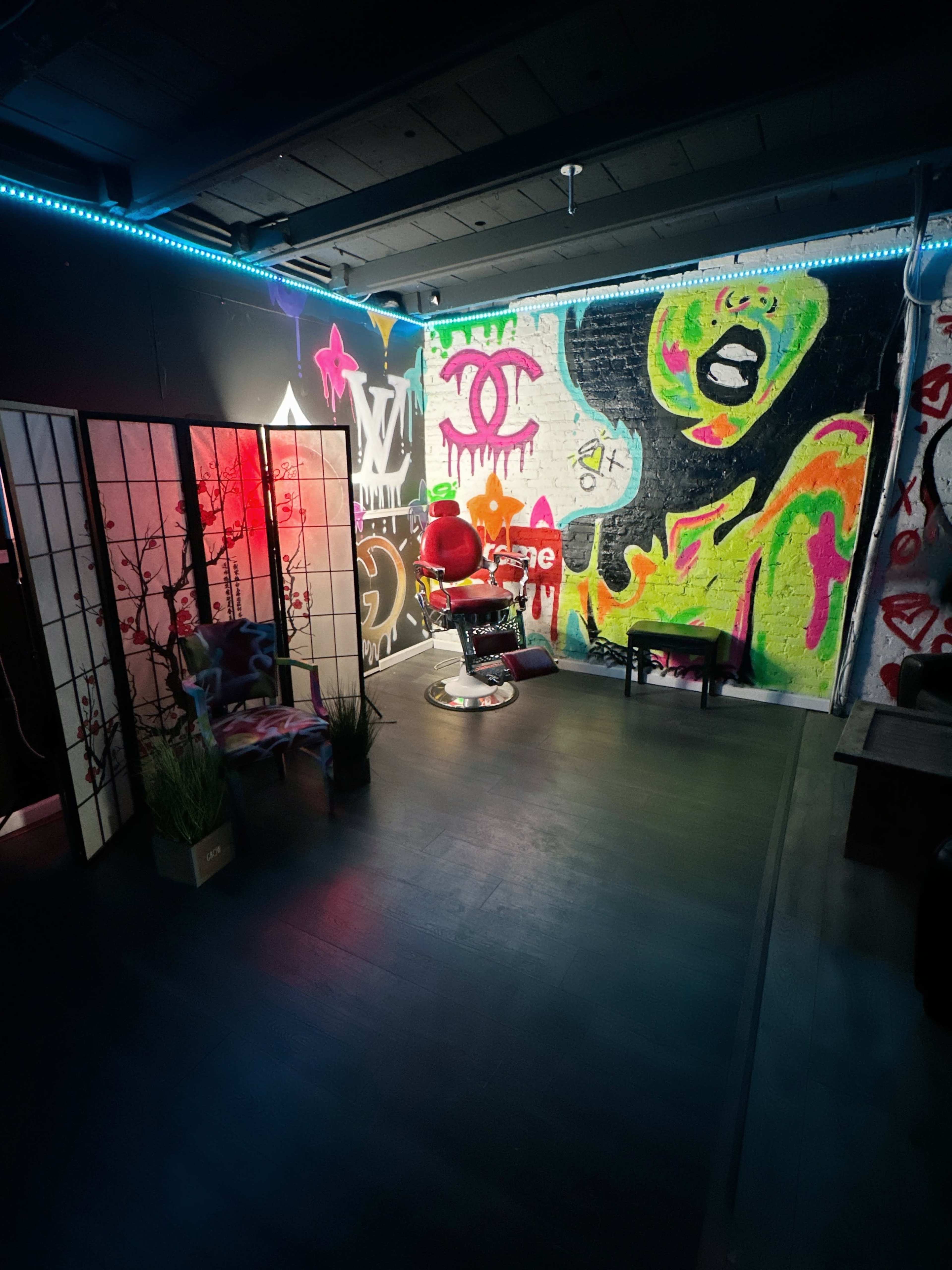 A vibrant tattoo parlor with a red tattoo chair, colorful graffiti on the wall, and minimalist seating in the corner.