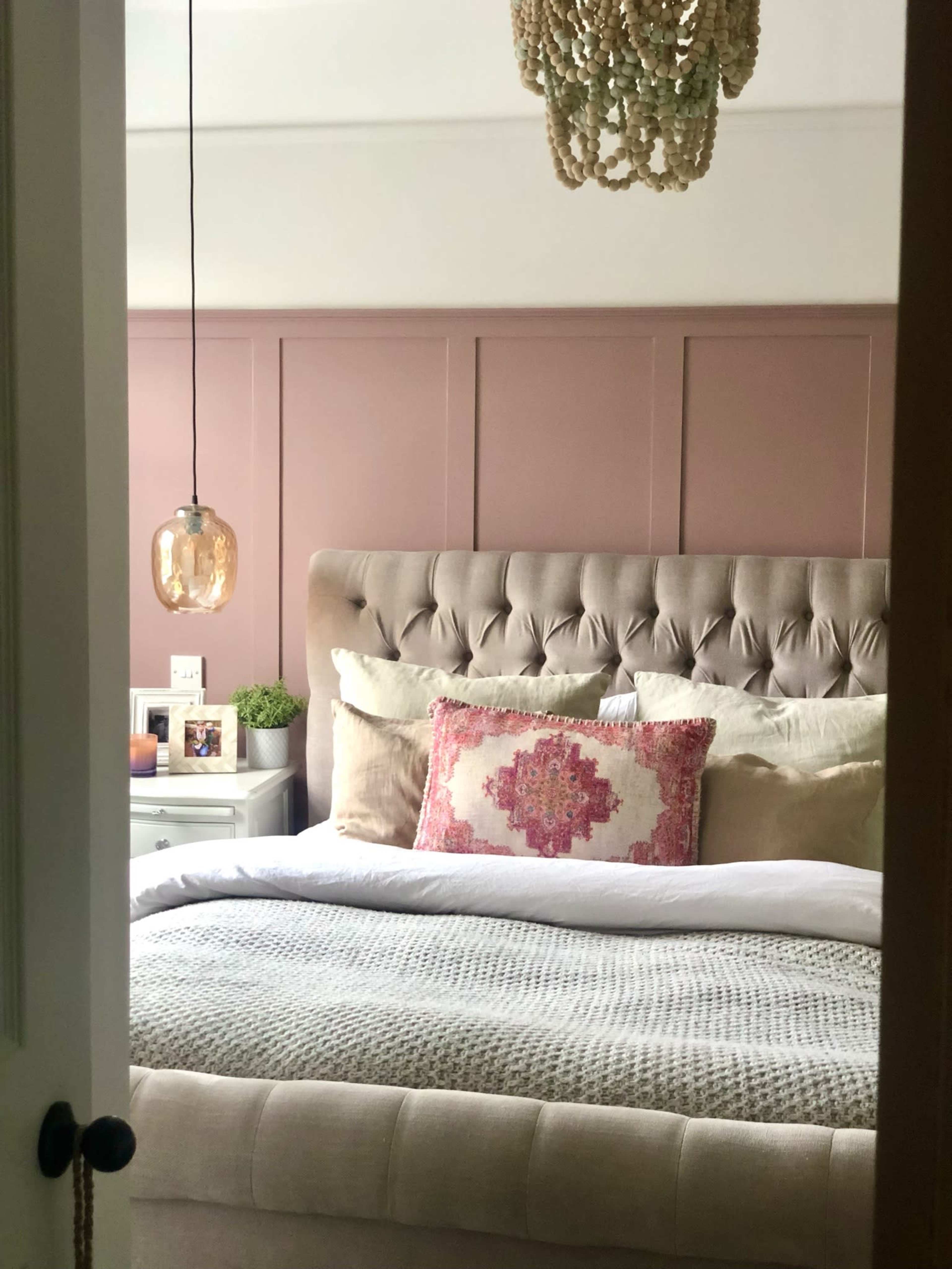A well-decorated bedroom features a tufted headboard, soft bedding, and a hanging light fixture, viewed through an open door.