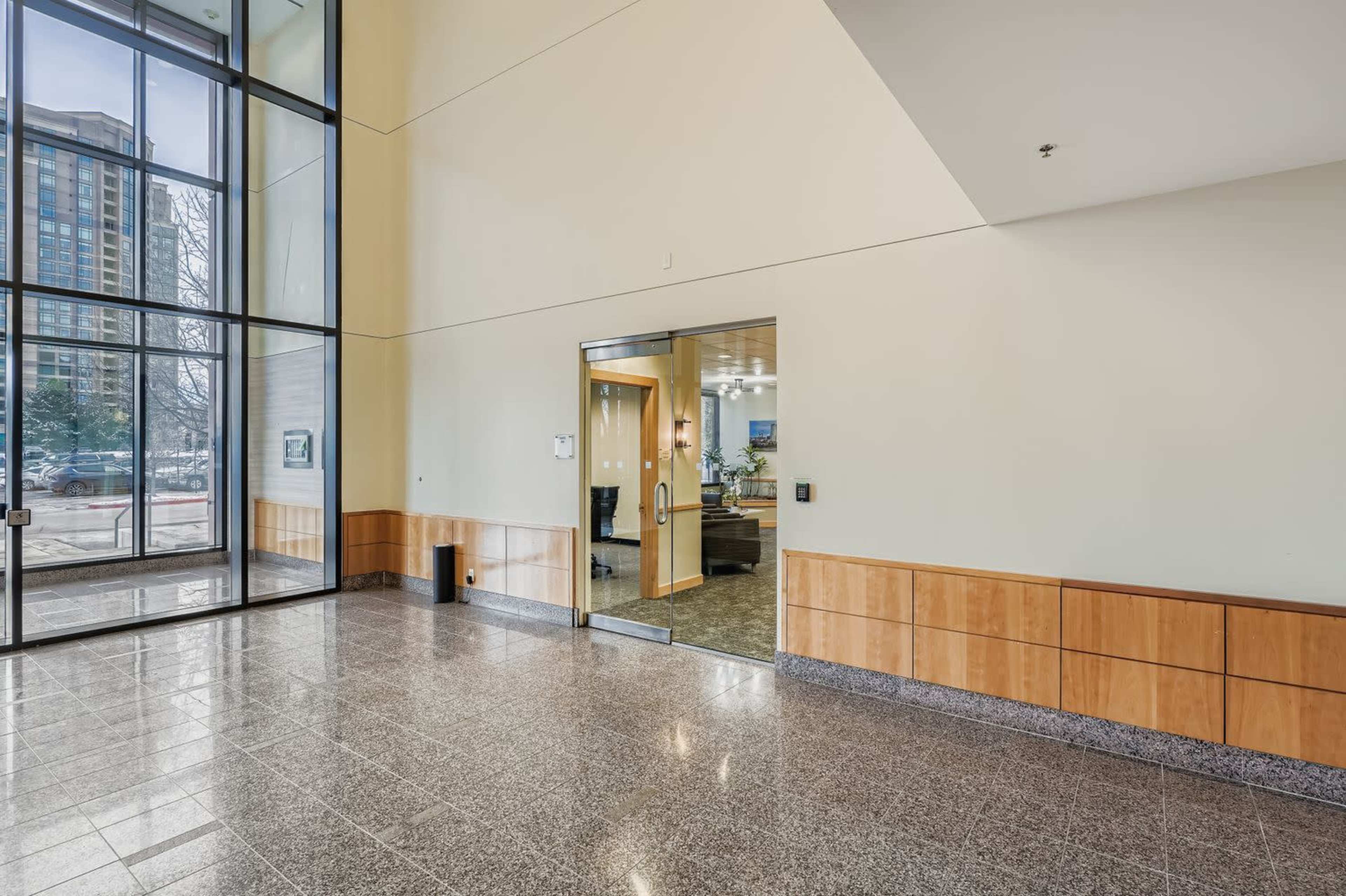 The image shows a spacious lobby area with large glass windows, leading to an open door that opens into another room.
