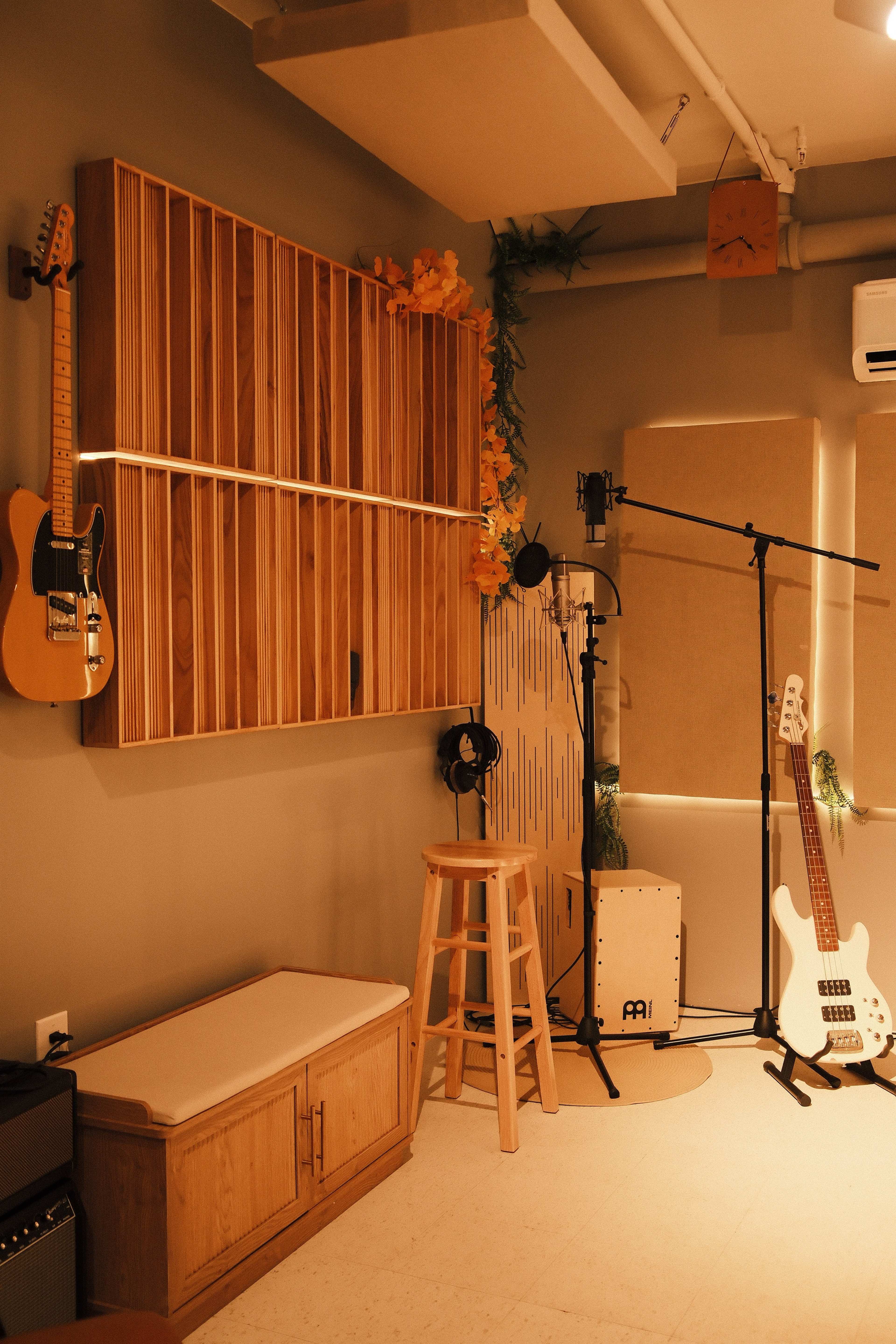 The image shows a music recording studio with wooden wall panels, guitars mounted on the wall, a stool, and various microphones set up.