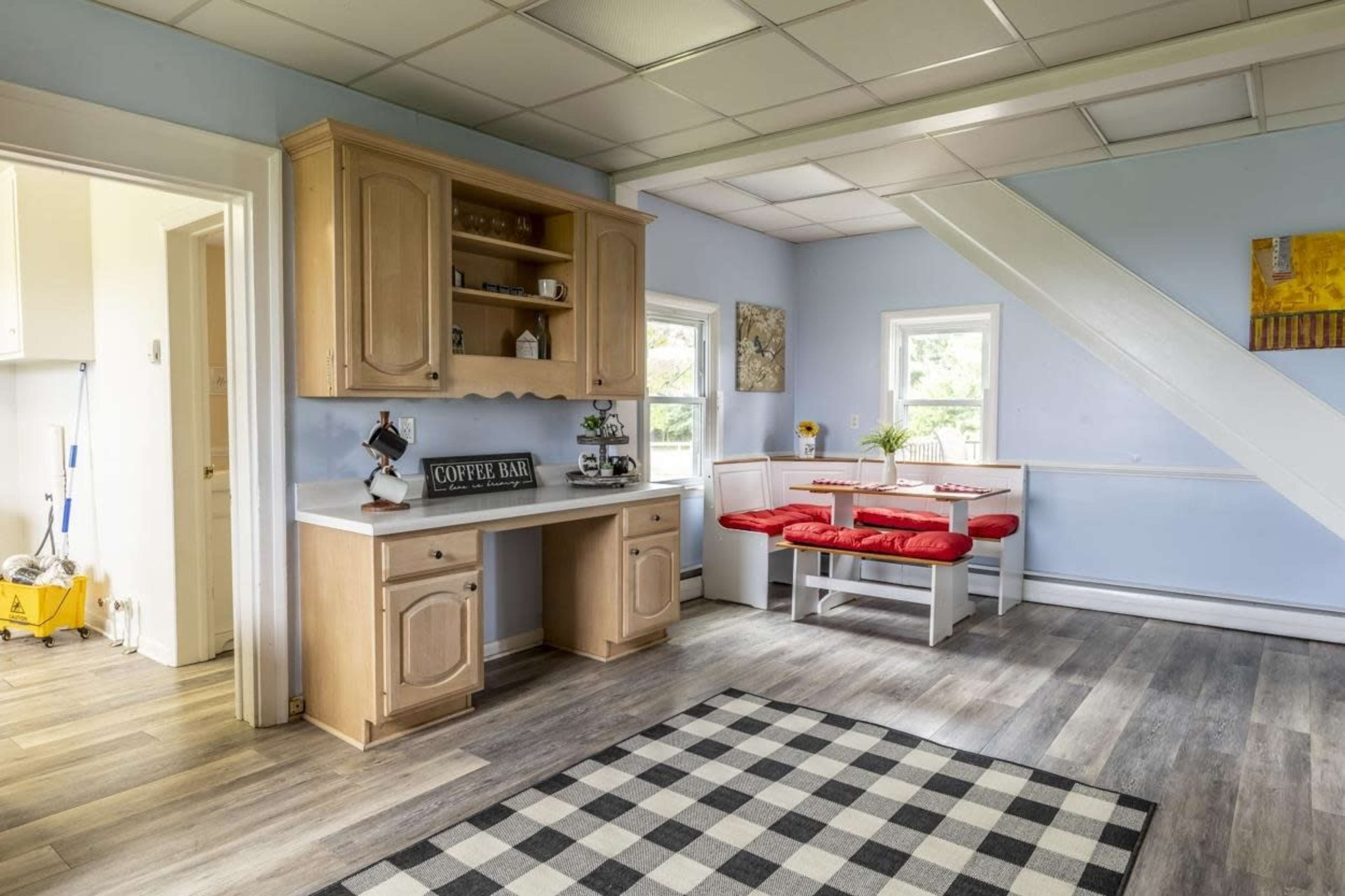 A light blue room featuring a coffee bar with wooden cabinetry, a small dining area with red seating, and a checkered floor.