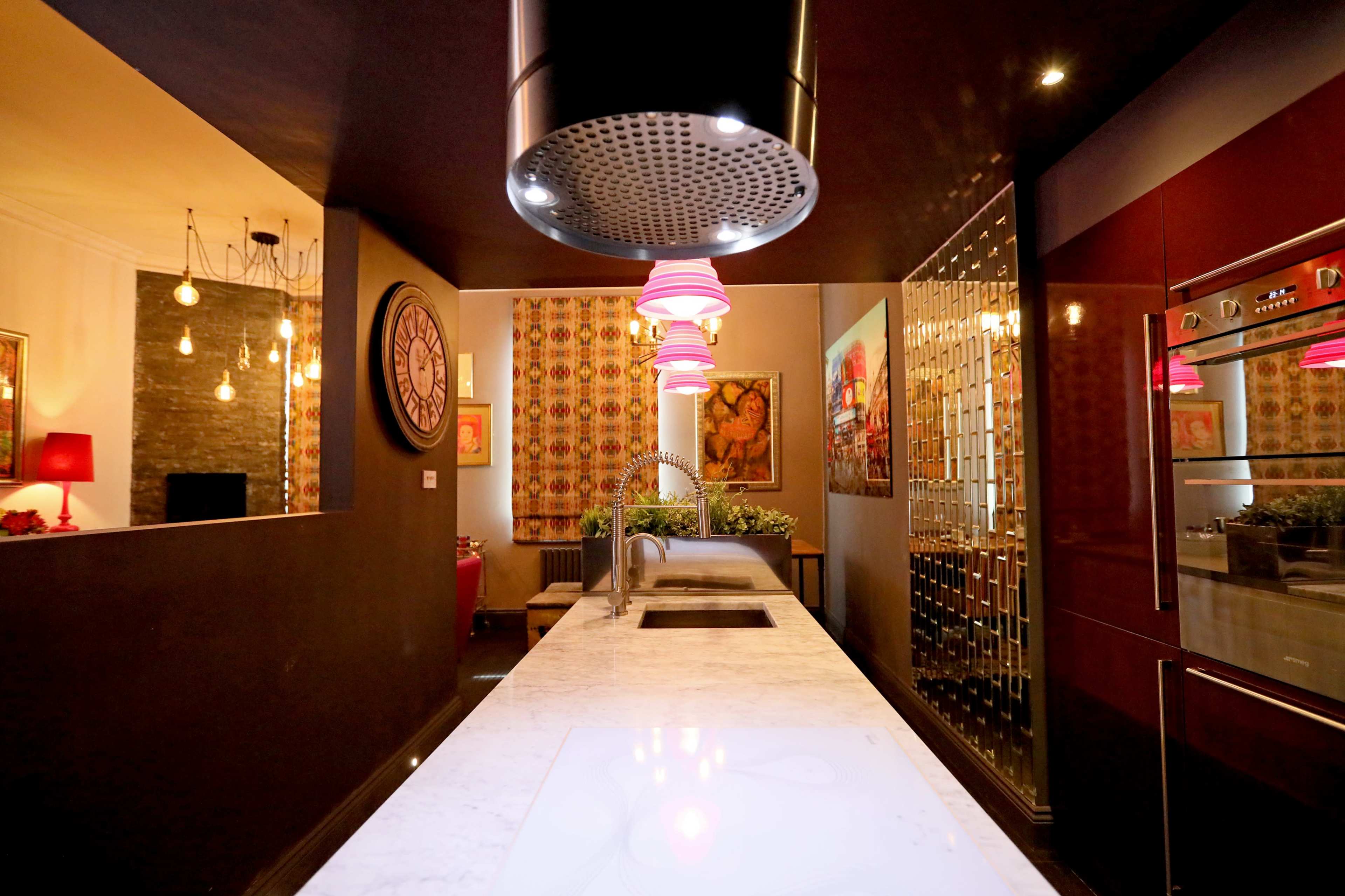 A modern kitchen with a marble island, pendant lighting, and colorful artwork on the walls.