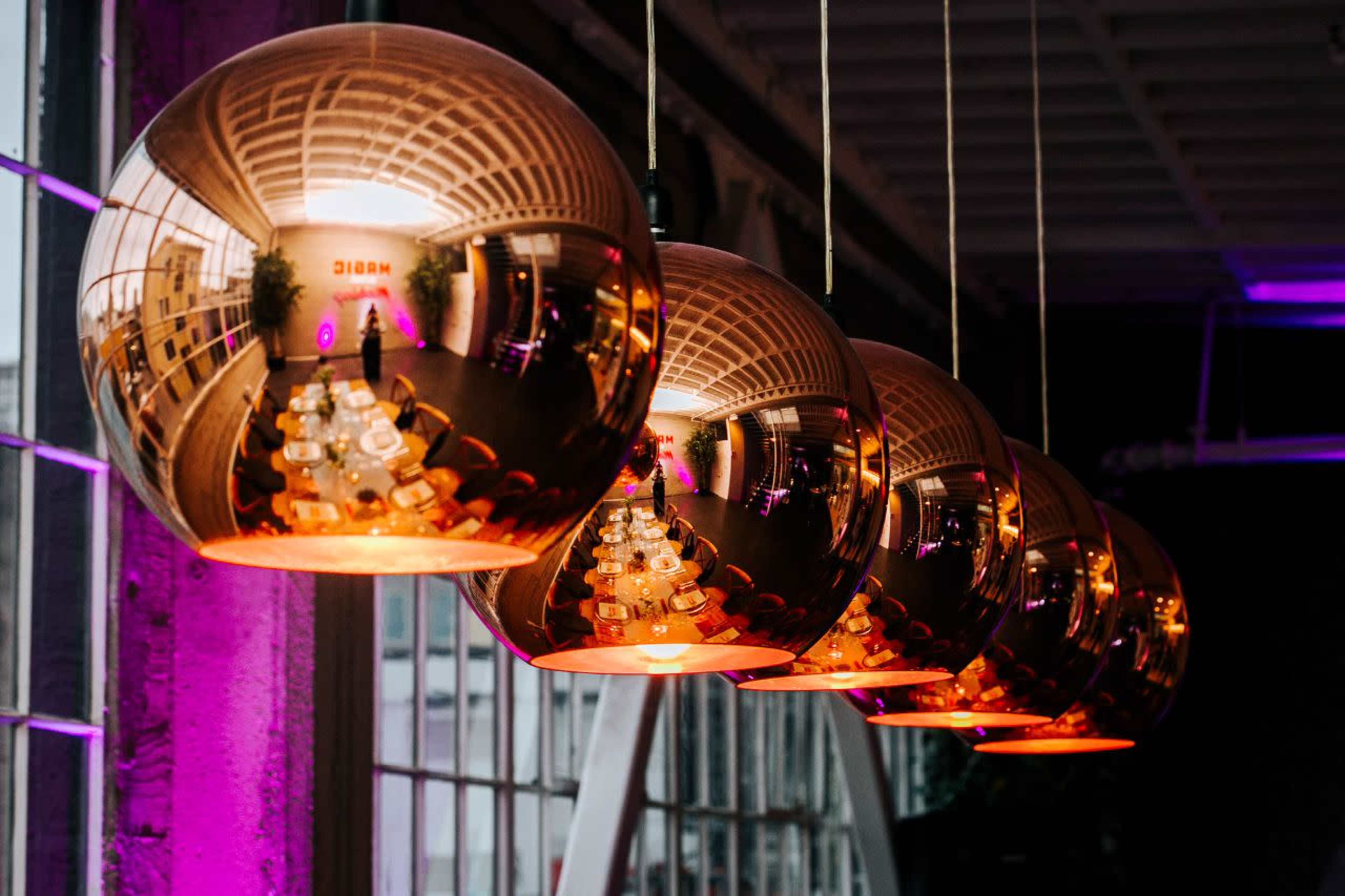 Five metallic pendant lights hang in a row, reflecting their surroundings and casting a warm glow.