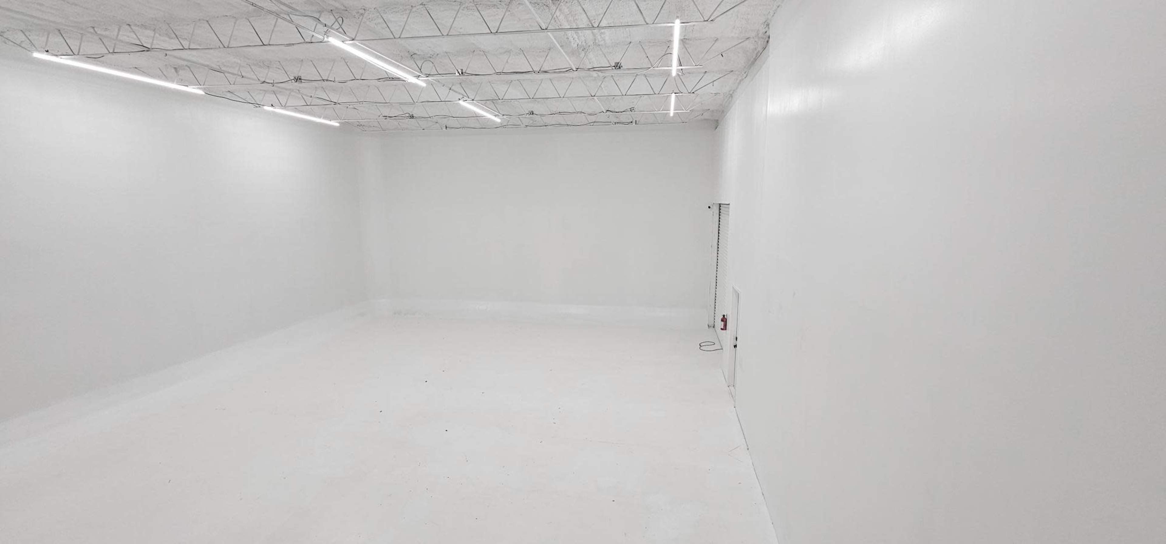 An empty, well-lit room with white walls and a ceiling, featuring a concrete floor.