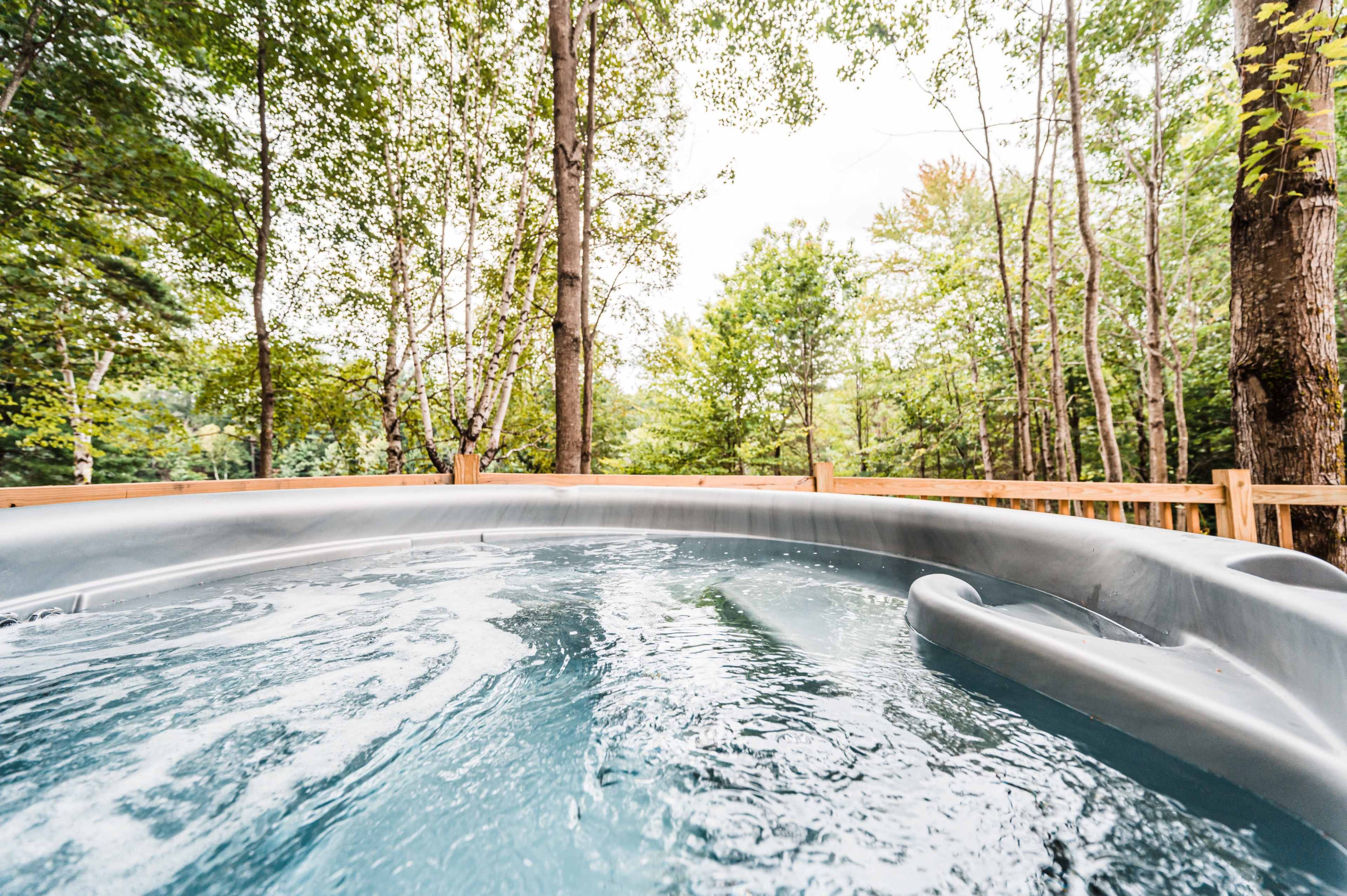 A hot tub filled with water sits on a wooden deck surrounded by trees.