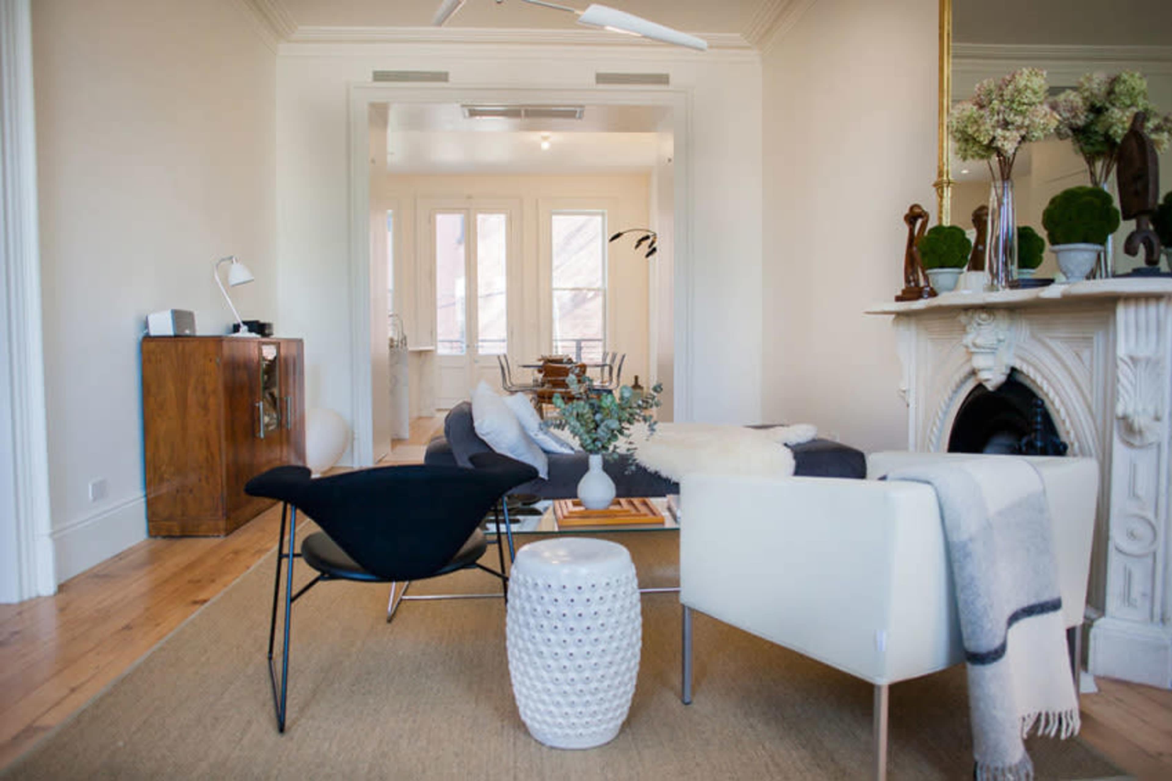 The image features a modern living room with a mix of furniture, including a black chair, a white chair, a coffee table, and a decorative side table, set against light-colored walls and hardwood flooring.