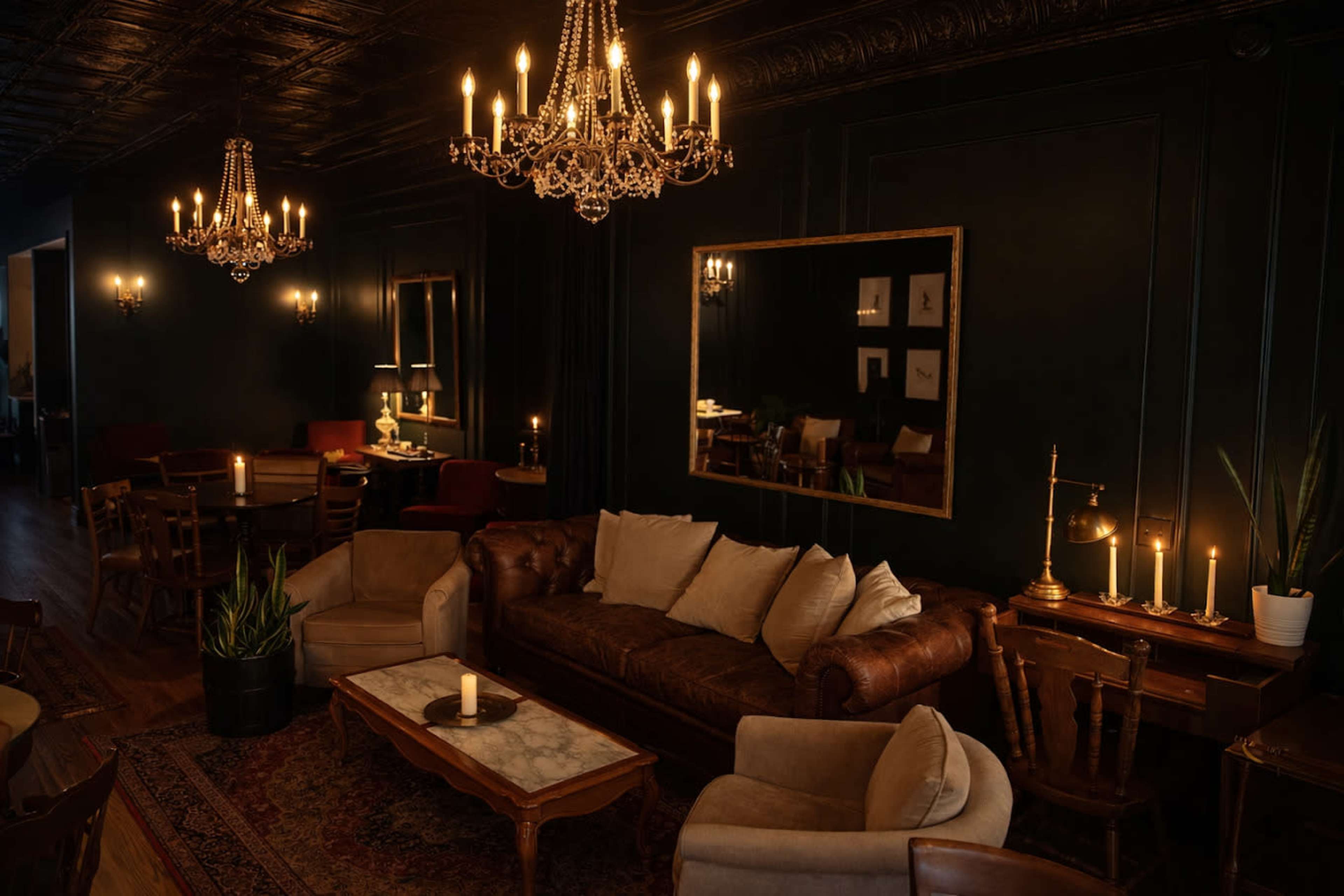 The image depicts a dimly lit, stylish lounge featuring leather sofas, elegant chandeliers, and a large mirror against dark walls.