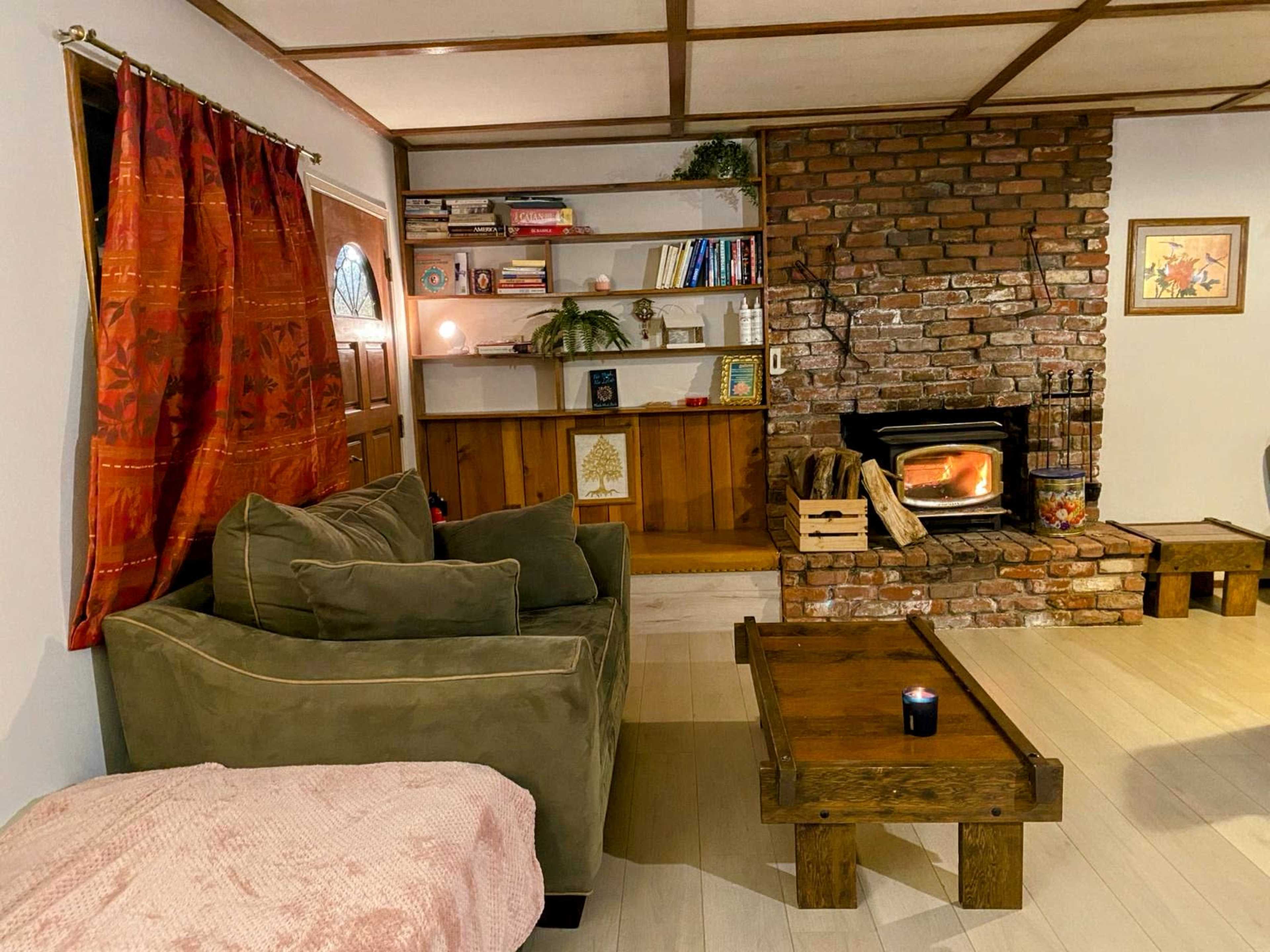 A cozy living room with a brick fireplace, a green couch, a wooden coffee table, and bookshelves filled with books.