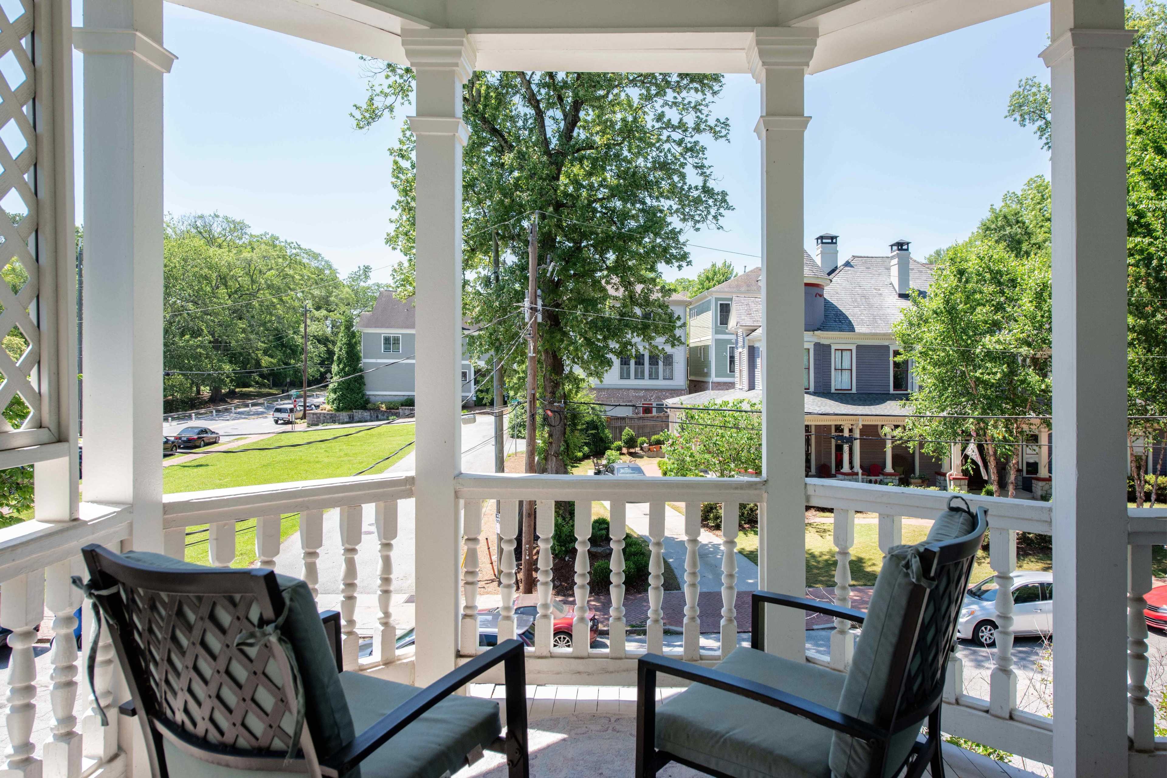 The image shows a porch with two chairs overlooking a street lined with parked cars and houses.