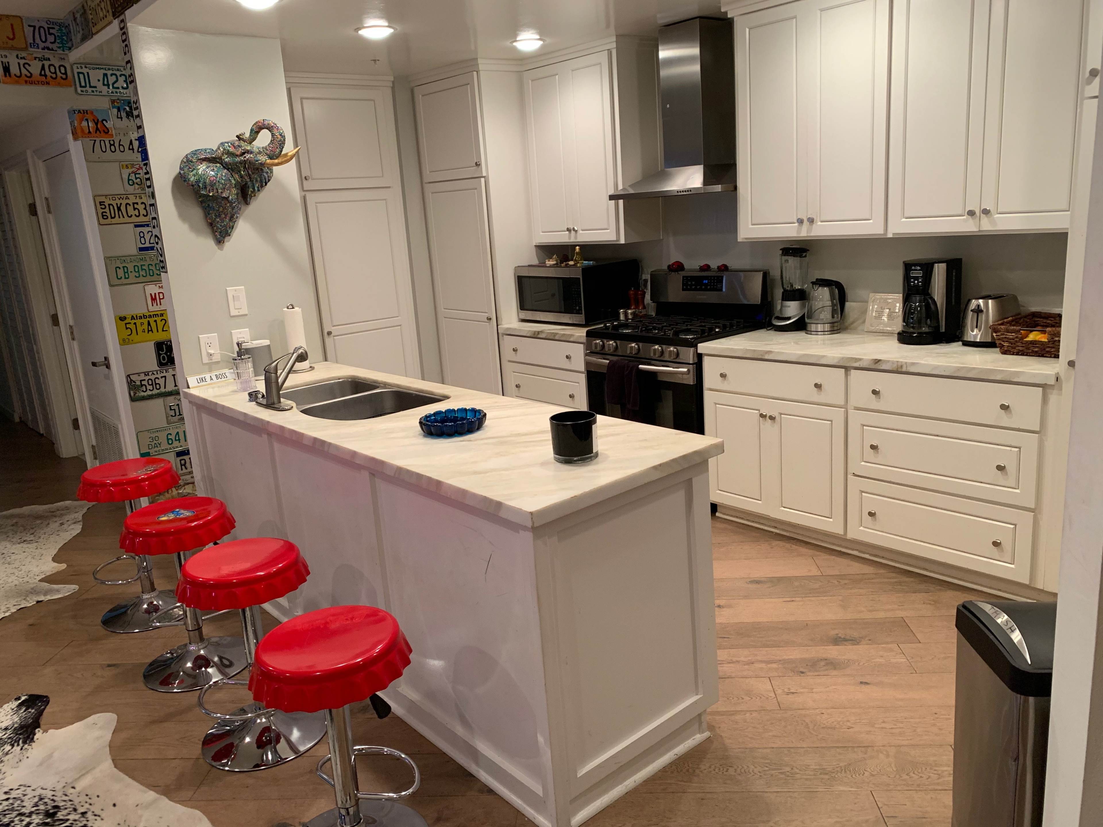 A modern kitchen with white cabinets, a marble countertop island with red stools, and stainless steel appliances.