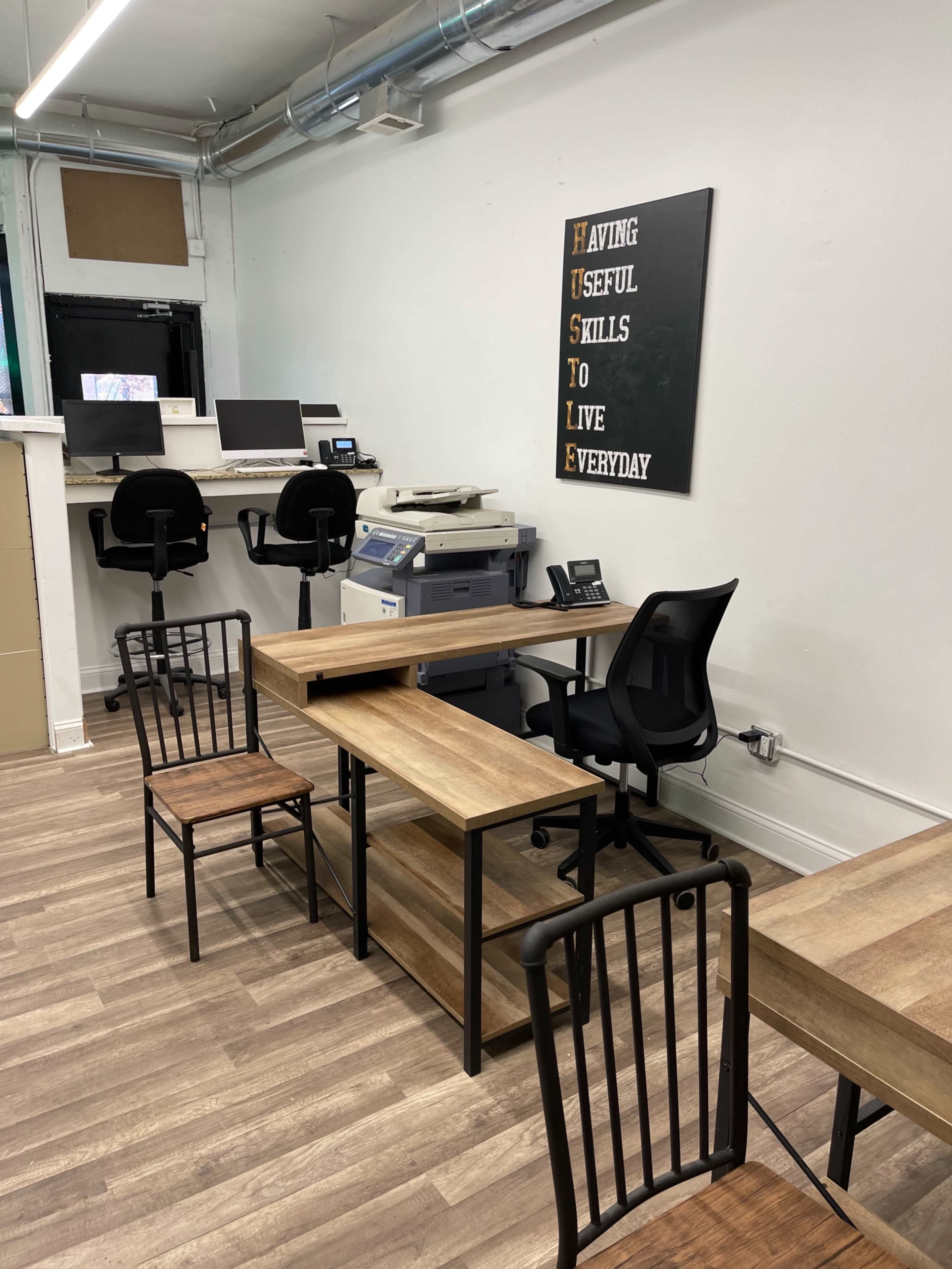 A minimalist office space with two tables and chairs, a printer, and two computers stationed against the wall.