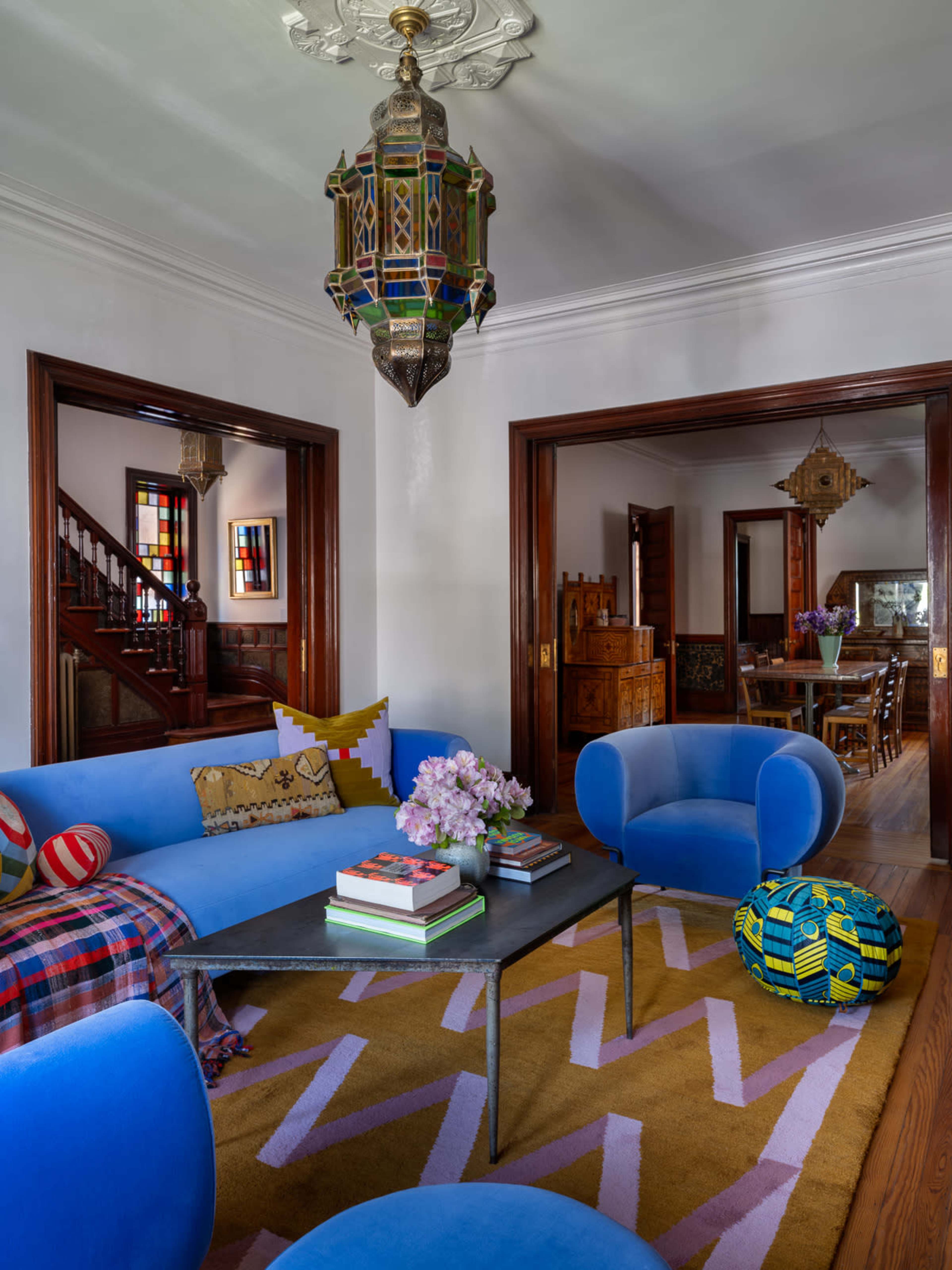 The living room features a blue couch and matching chairs around a coffee table, with colorful patterns in the decor and a decorative lantern hanging from the ceiling.